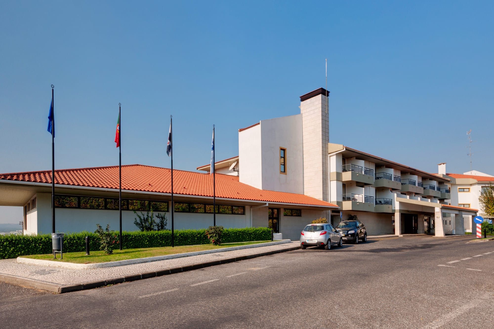 Hotel building exterior, red tile roof, balconies, Portuguese flag, parking.