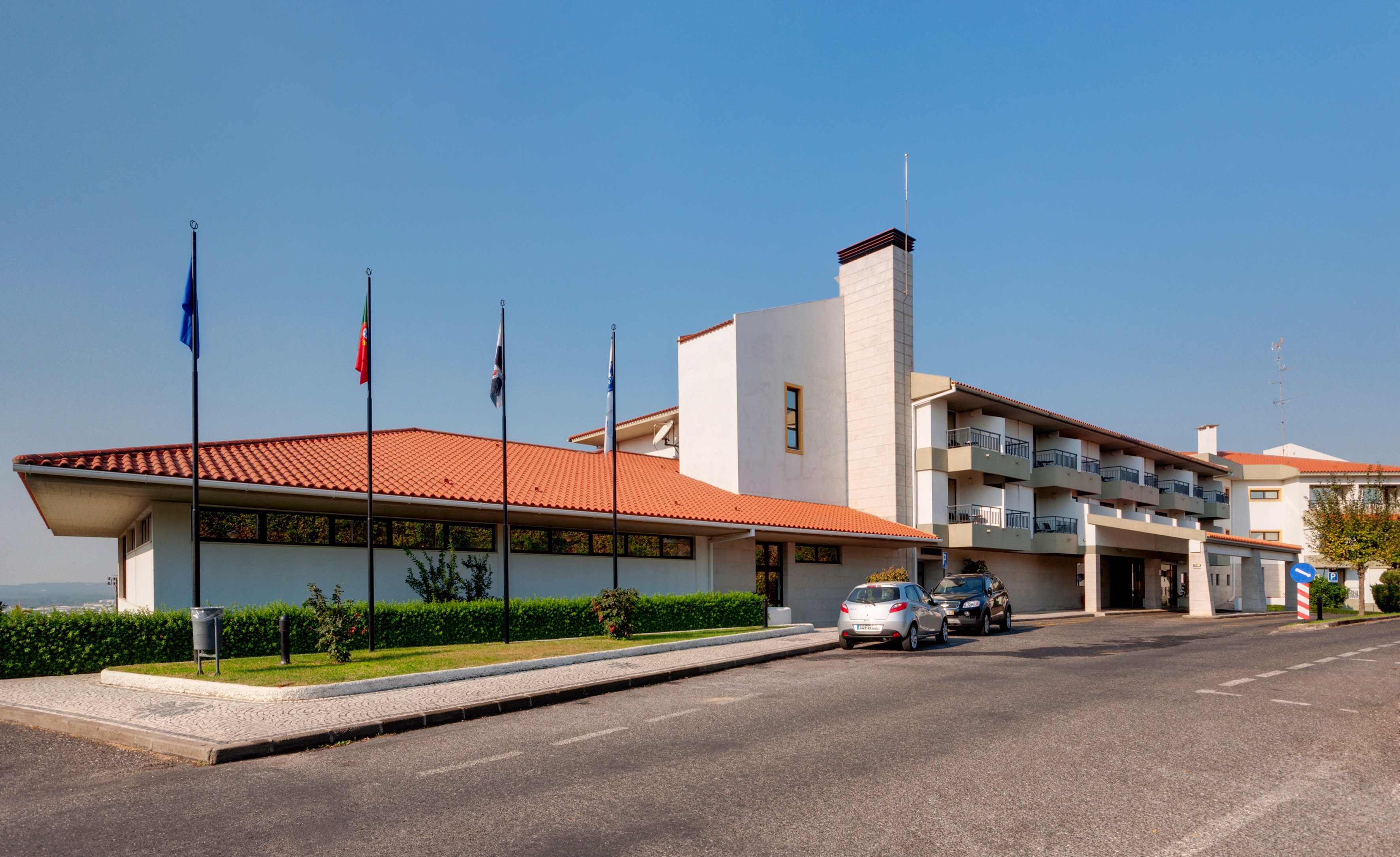 Hotel building exterior, red tile roof, balconies, Portuguese flag, parking.