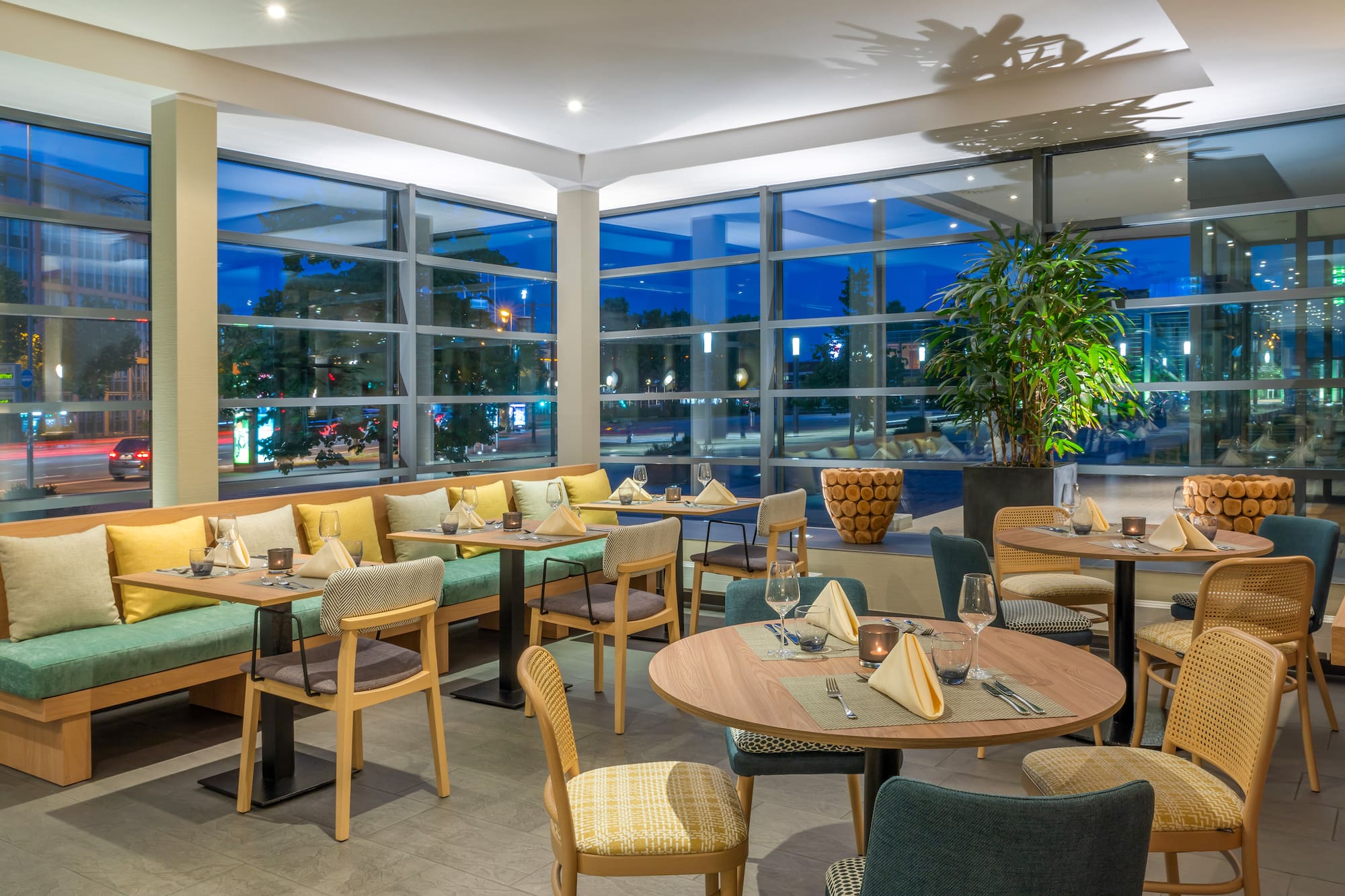 Modern restaurant dining room, set tables, booth seating, city evening view.