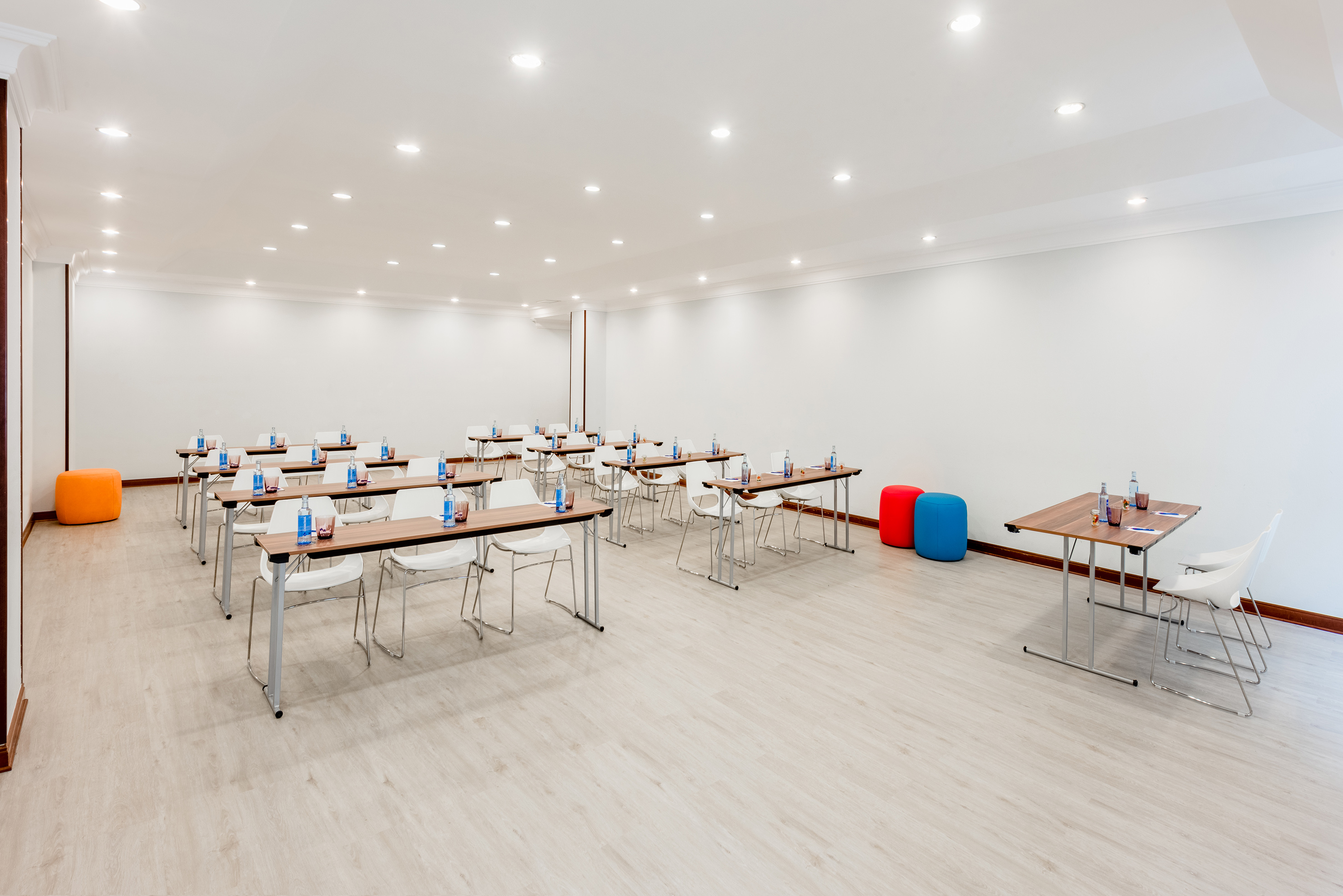 Modern meeting room, classroom setup, light wood floor, white chairs, bright.