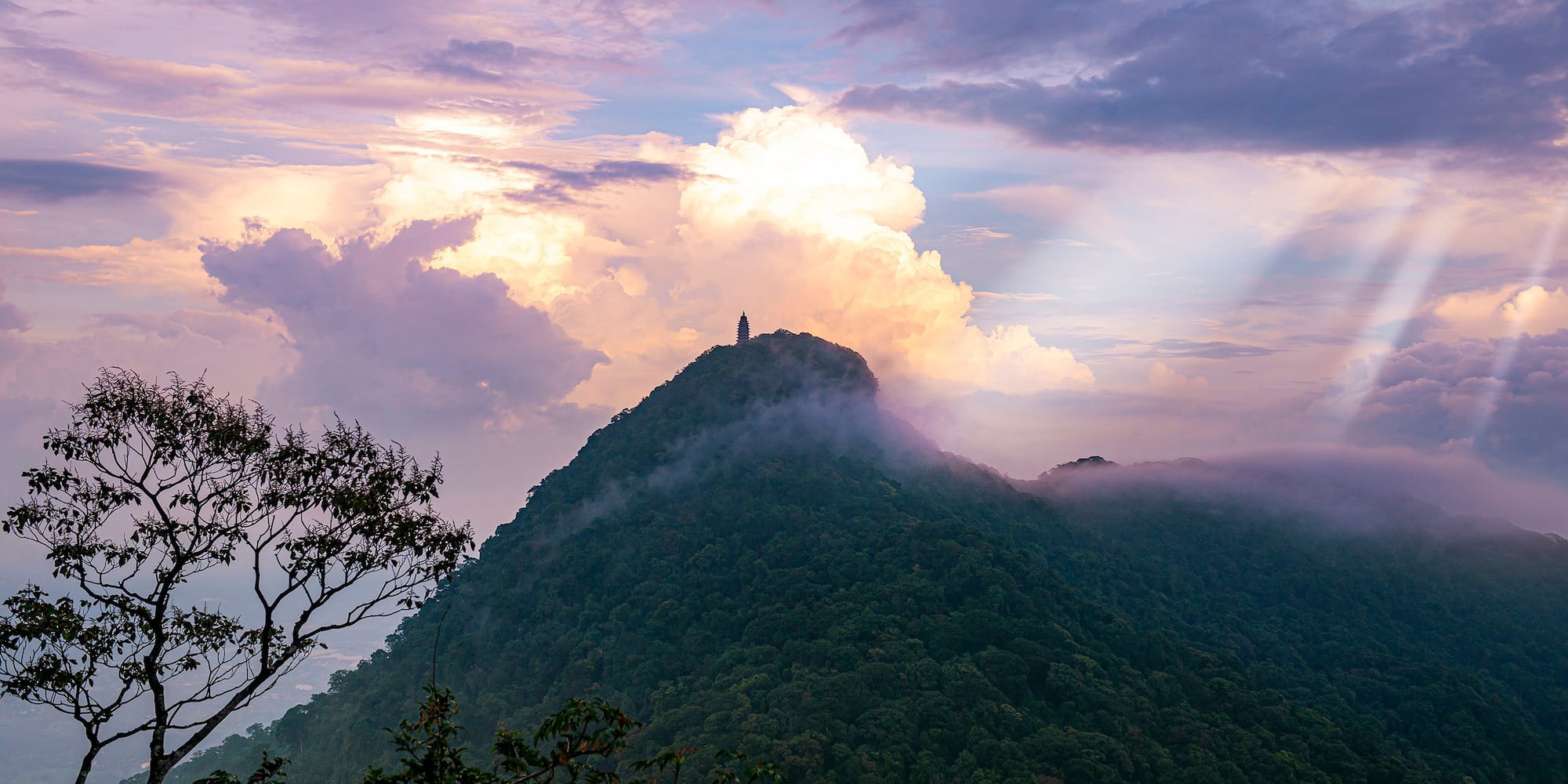a mountain with clouds and a tower on top
