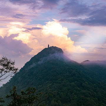 a mountain with clouds and a tower on top