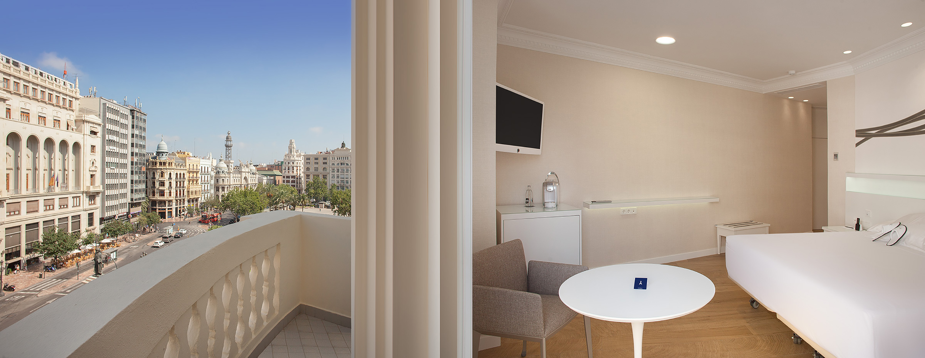 Modern hotel room with balcony, city street view, and classic buildings.