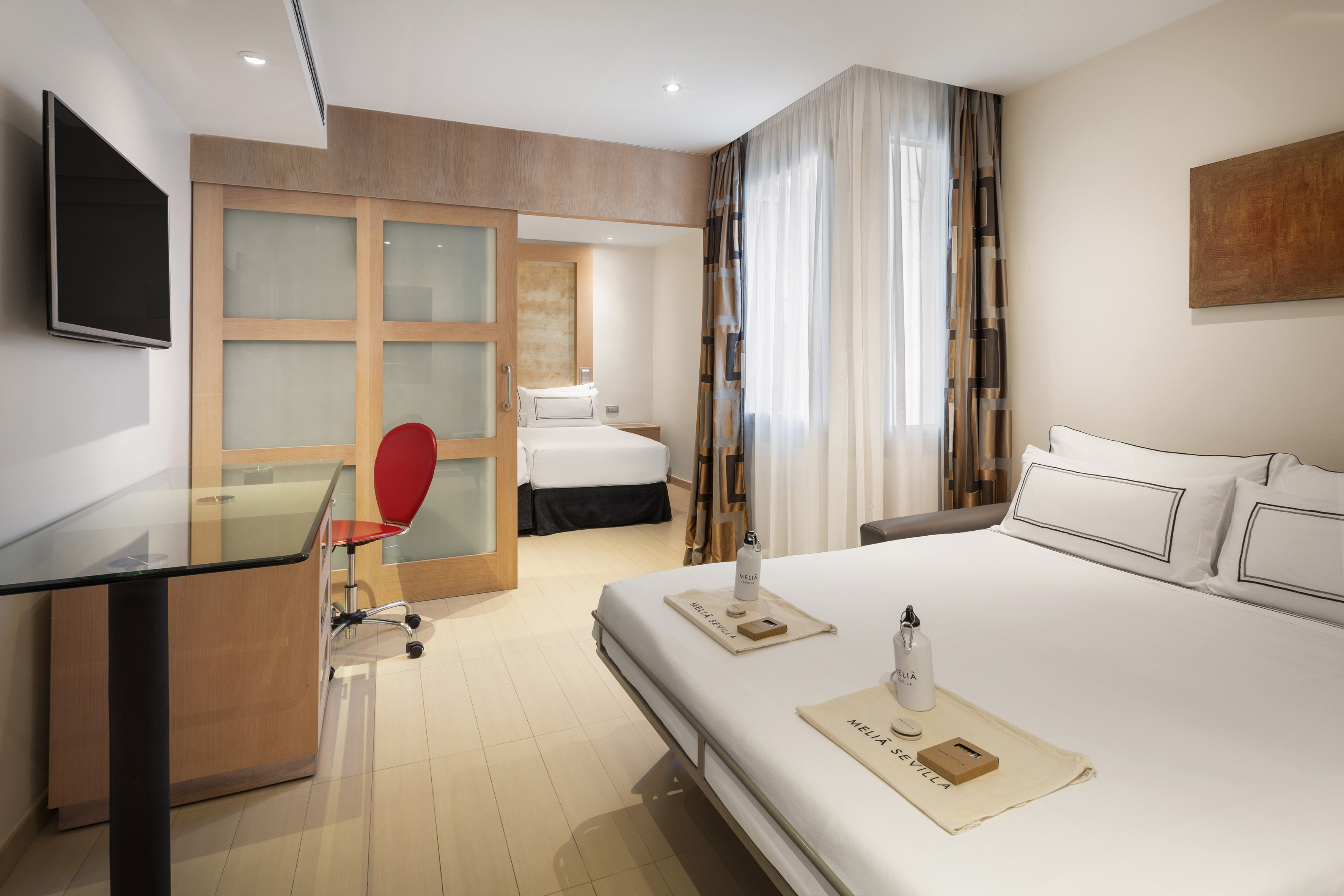 Meliá Sevilla hotel room with main bed, desk, TV, and separate guest bed area.