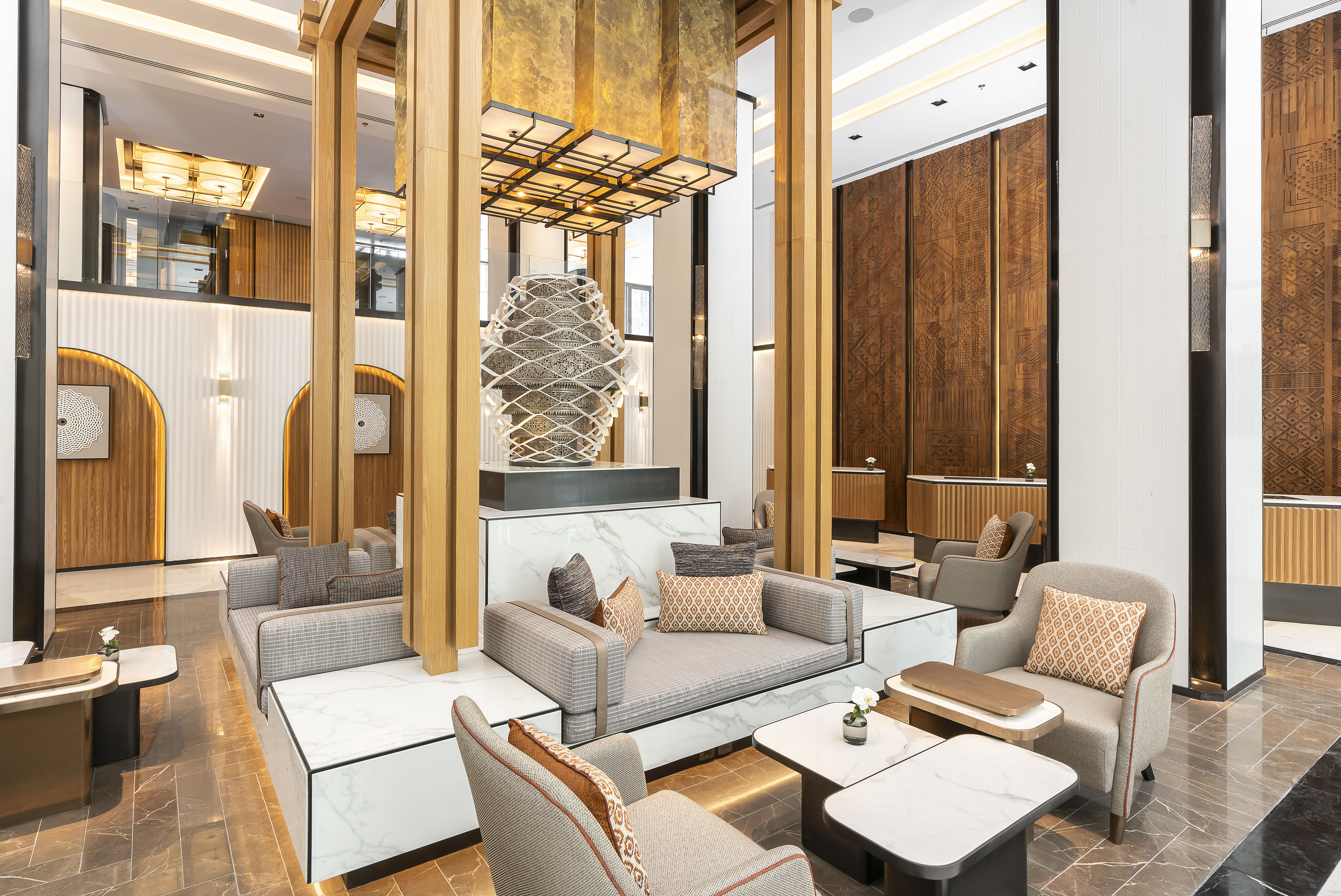 Luxury hotel lobby with modern seating, central sculpture, wood, and marble.