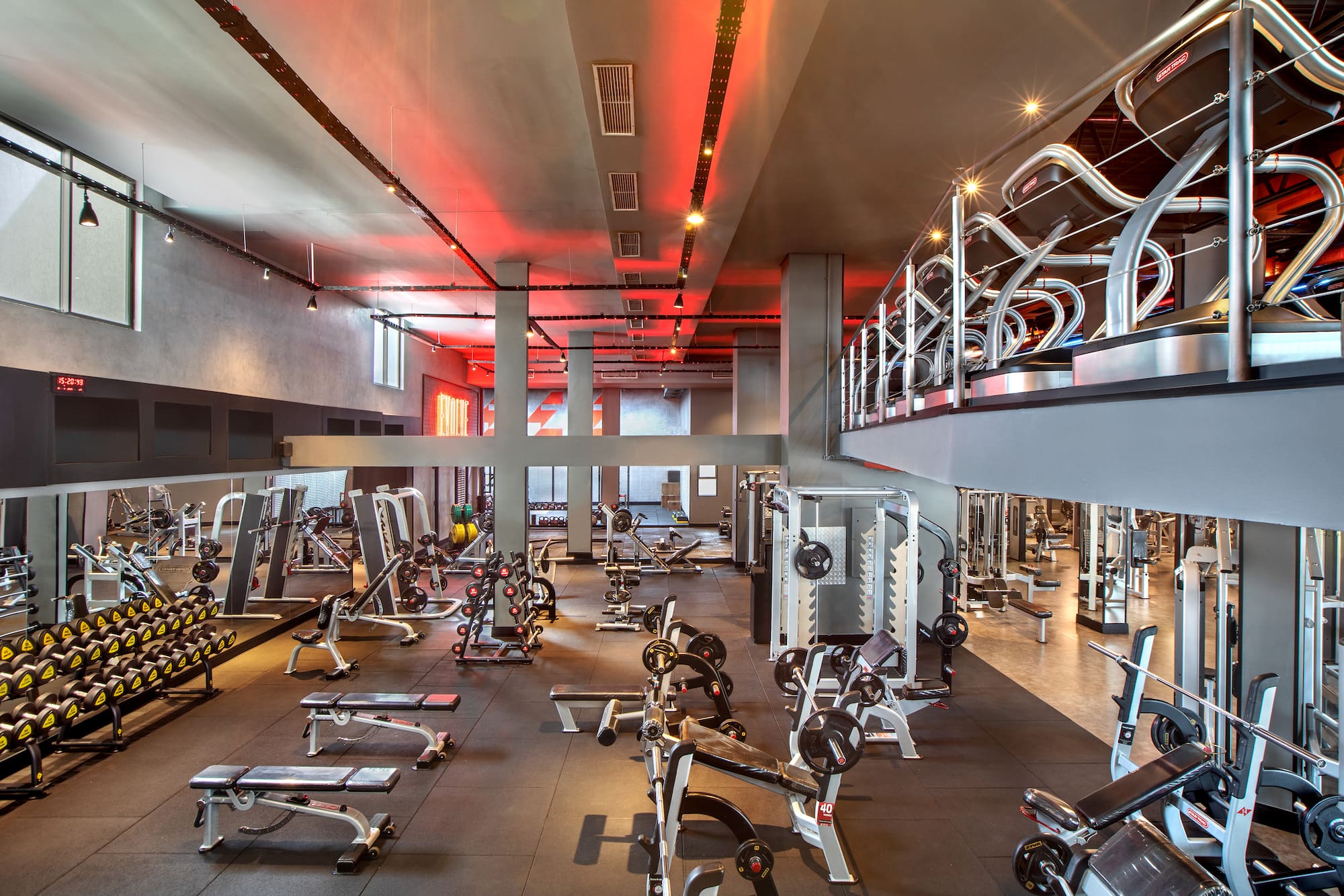 Modern gym interior with red lighting, weight machines, and treadmills.