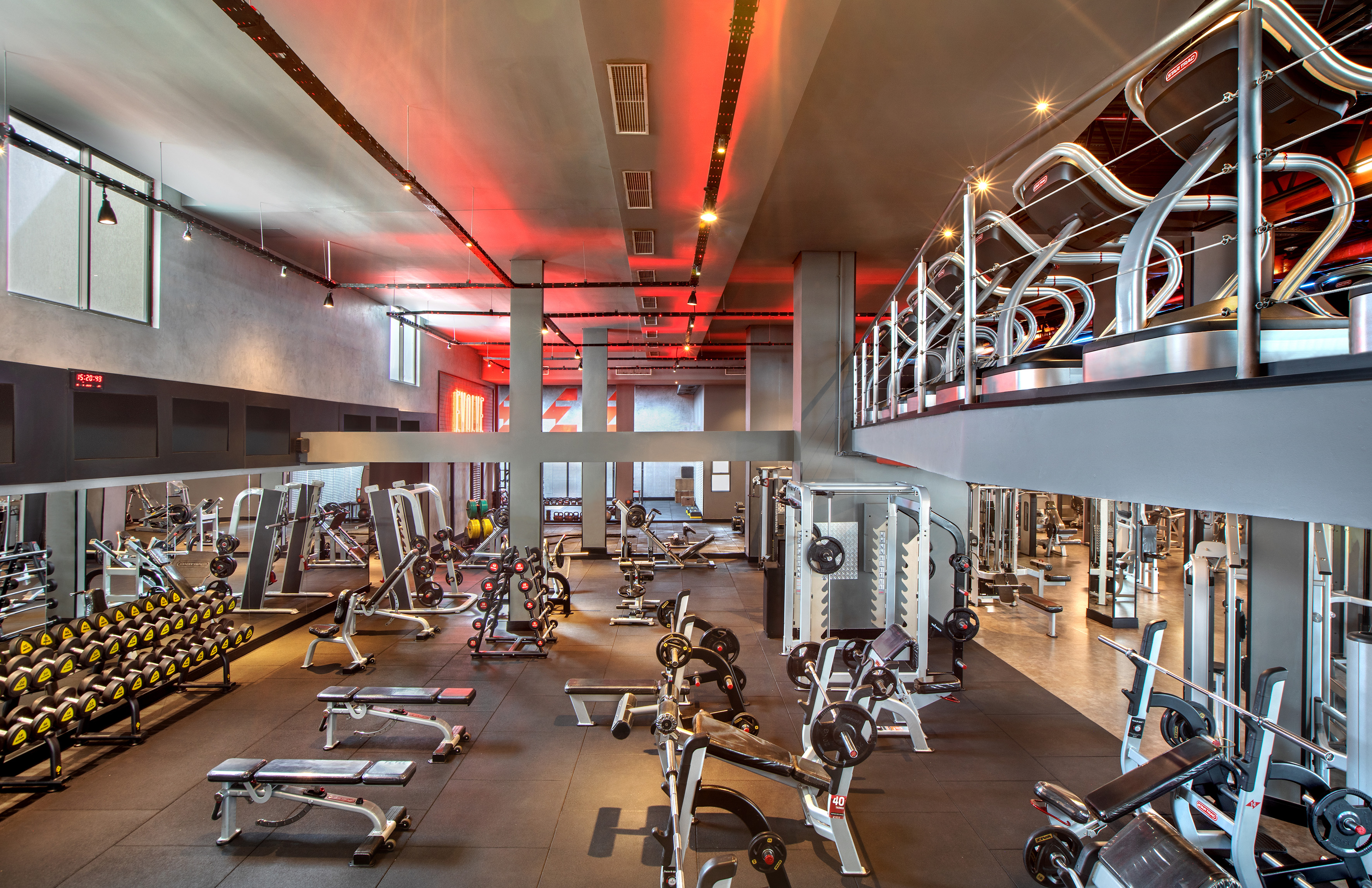 Modern gym interior with red lighting, weight machines, and treadmills.