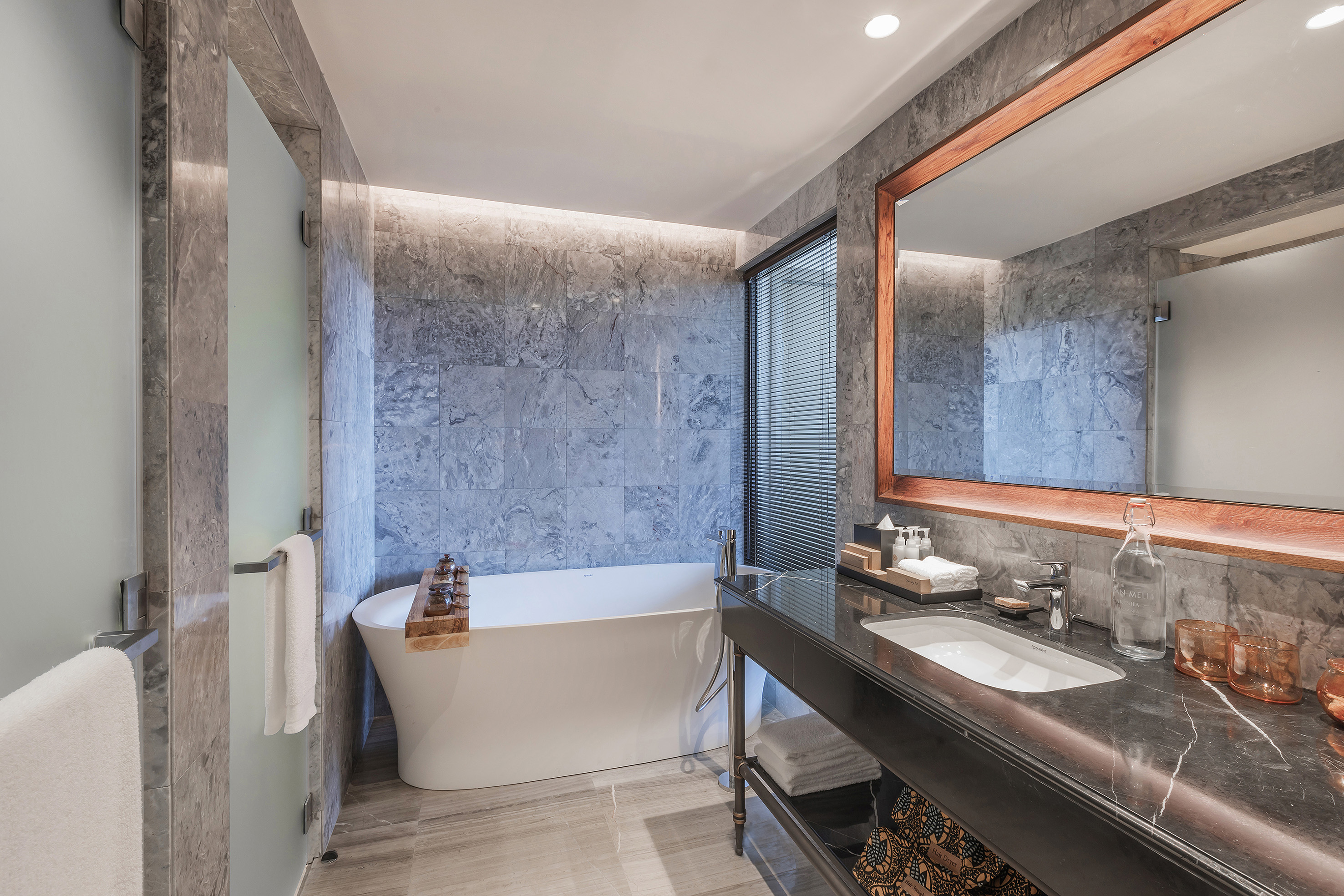 Sleek luxury bathroom with freestanding tub, grey marble walls, and dark vanity.