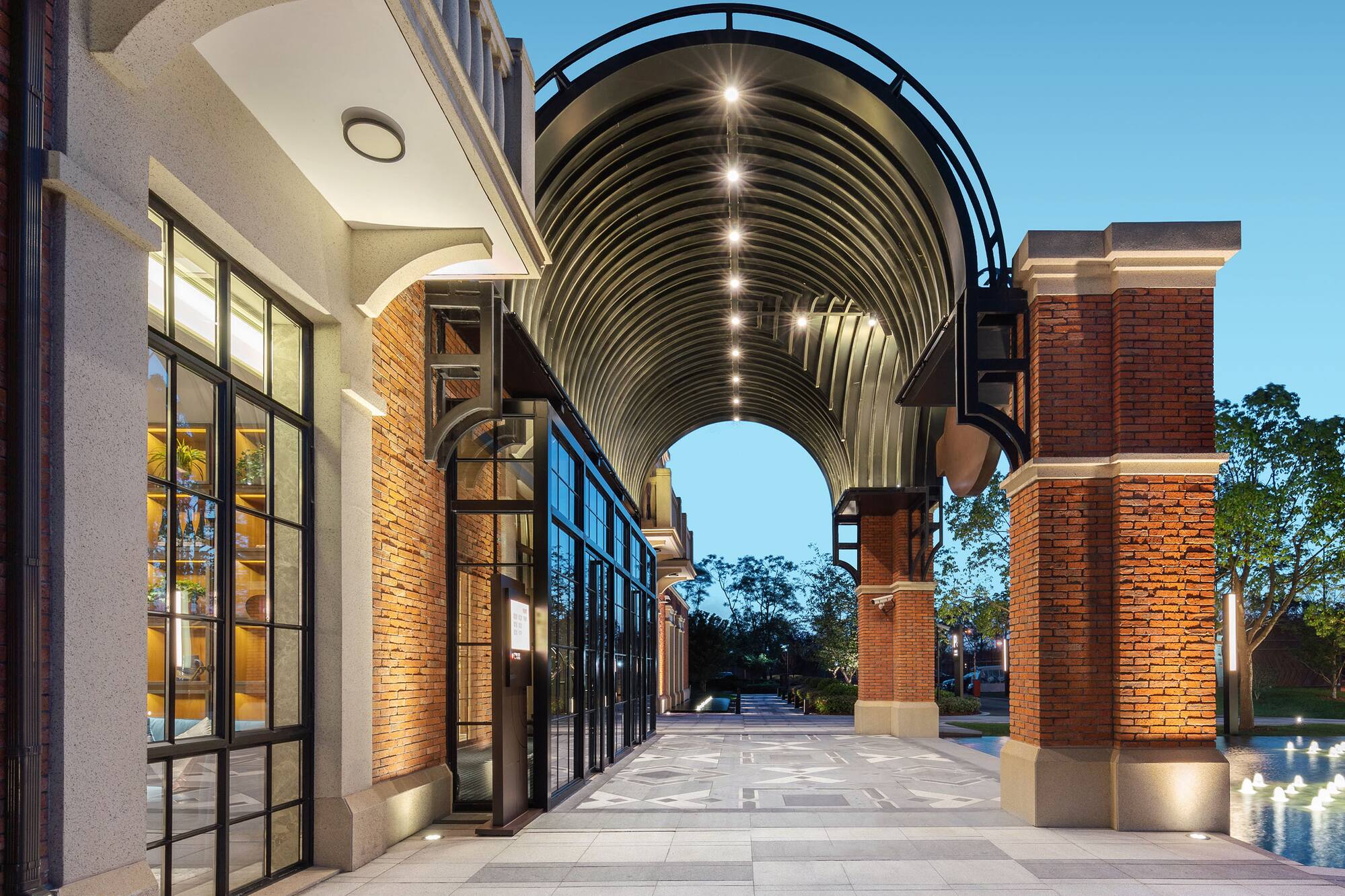Illuminated architectural walkway with modern brick buildings, arched canopy.