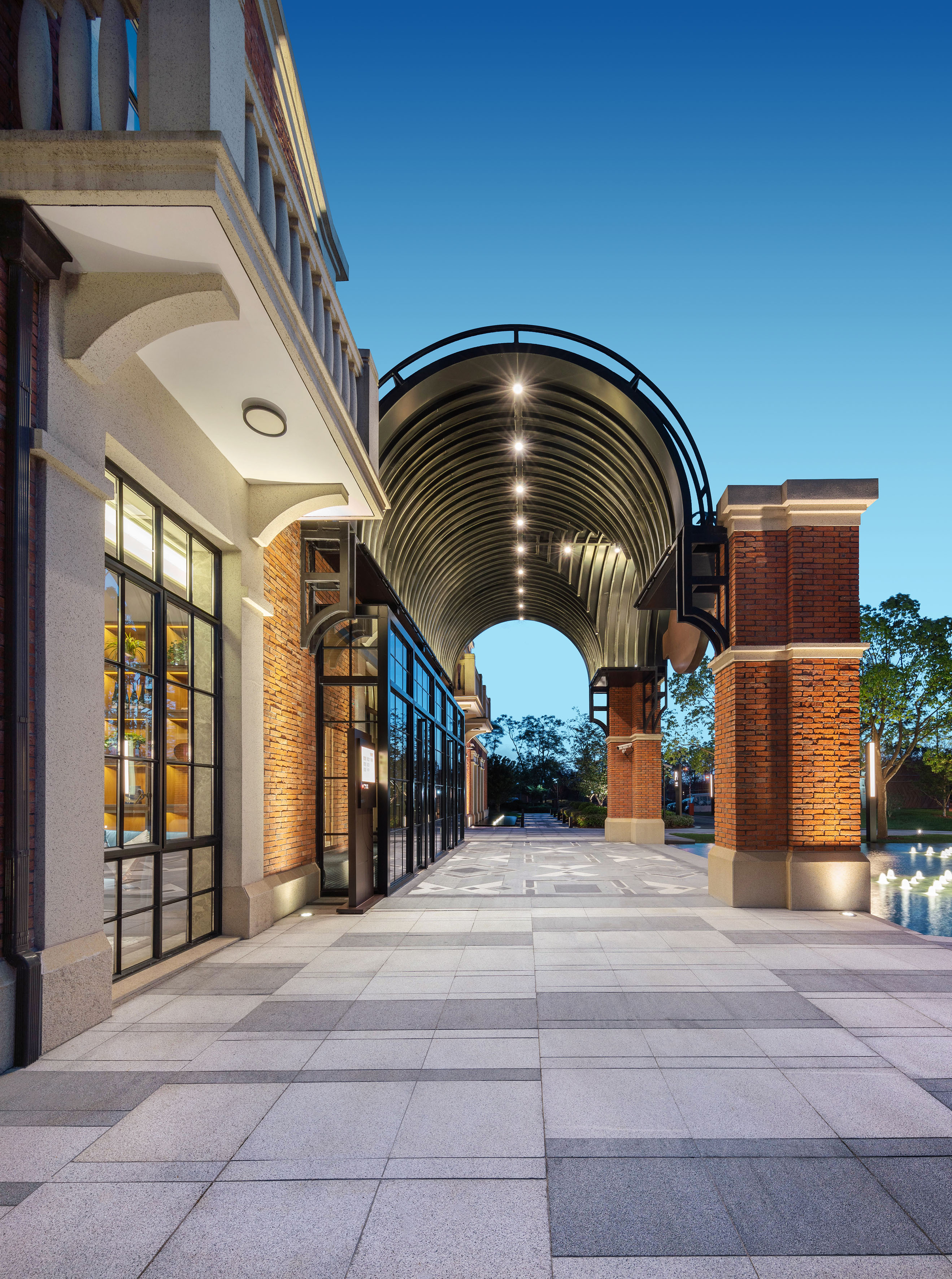 Illuminated architectural walkway with modern brick buildings, arched canopy.
