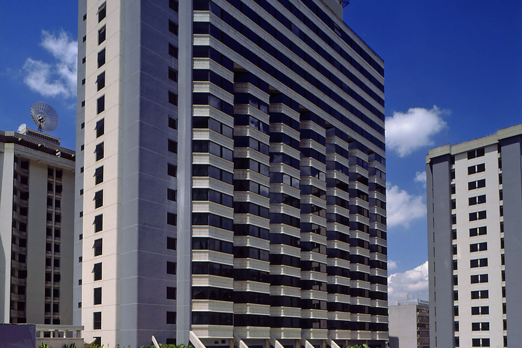 Modern high-rise hotel with outdoor resort pool, fountain, and sun loungers.
