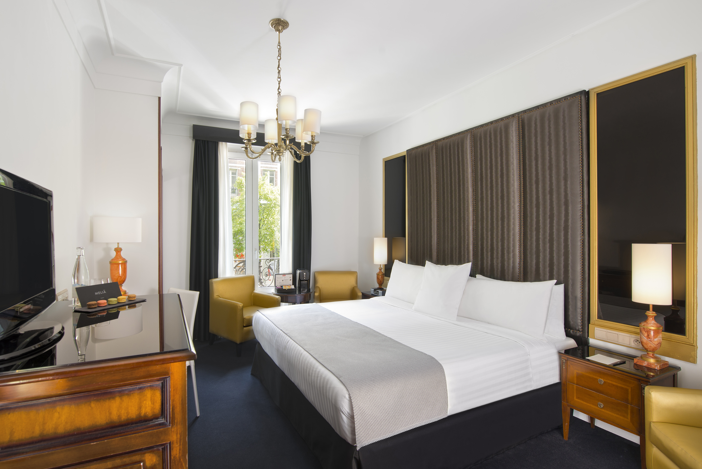Elegant hotel bedroom with king bed, yellow chairs, and classic chandelier.