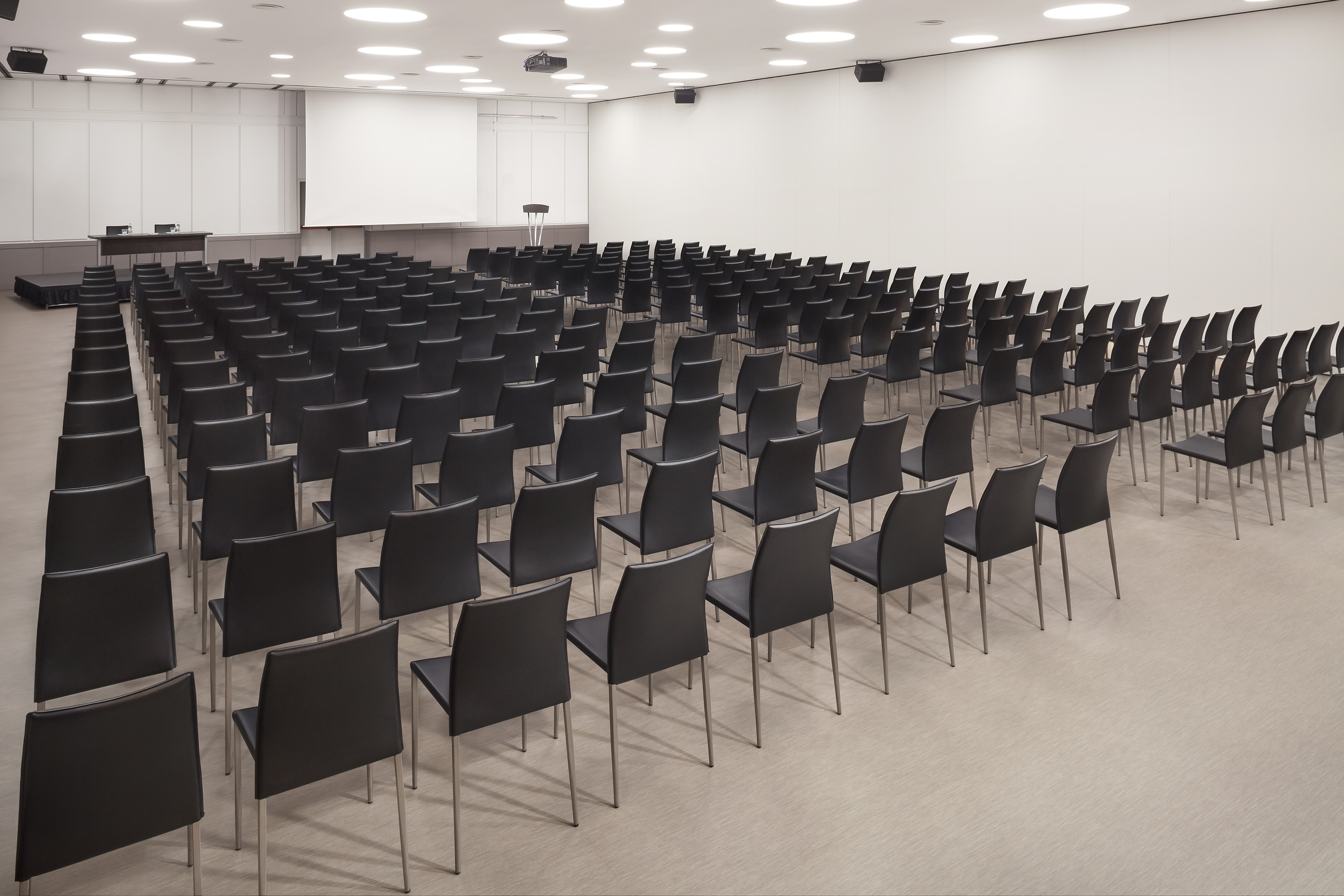 Conference room with black chairs, large screen, and lectern setup.