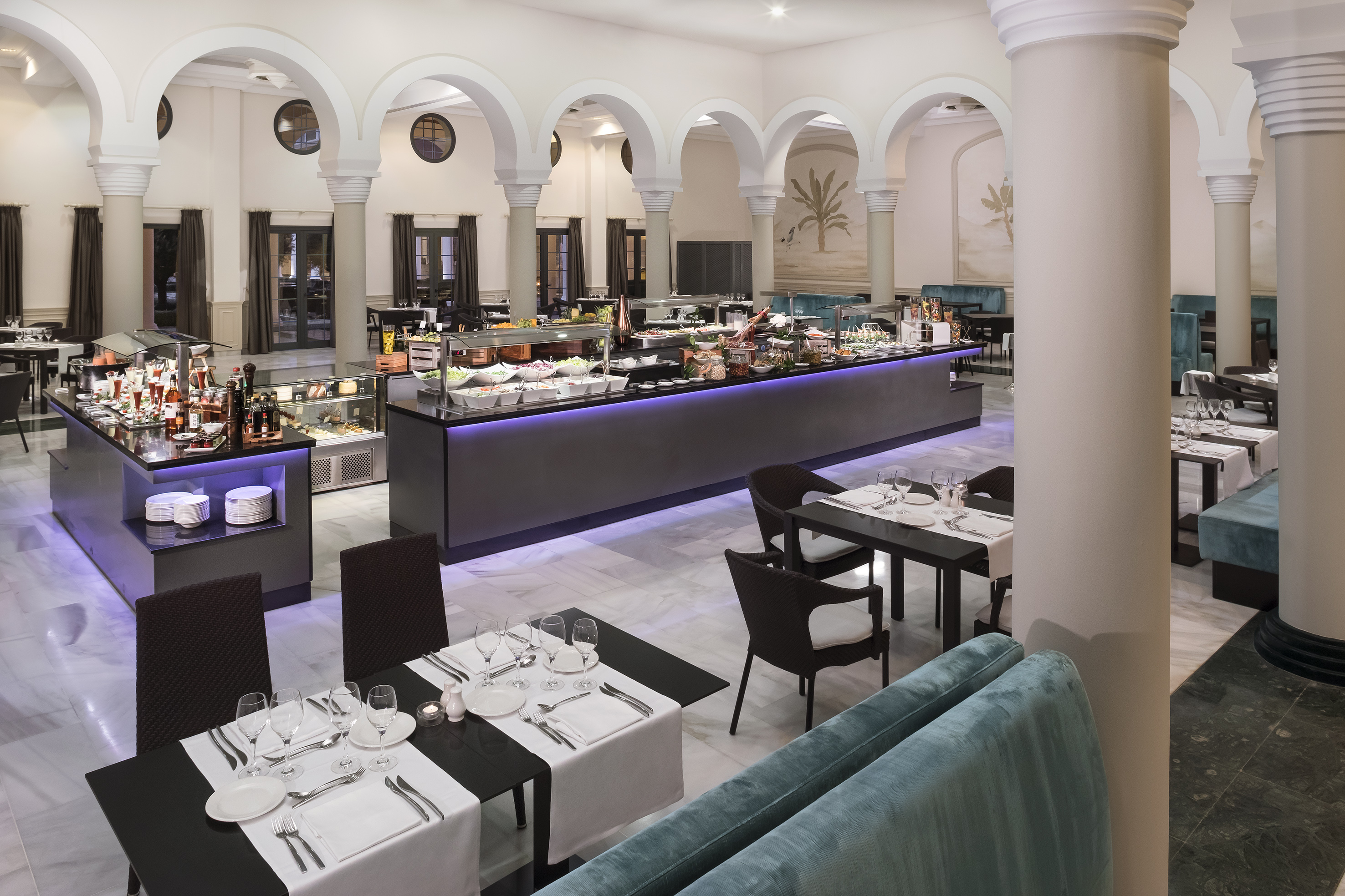 Elegant hotel buffet restaurant with diverse food displays and set dining tables.
