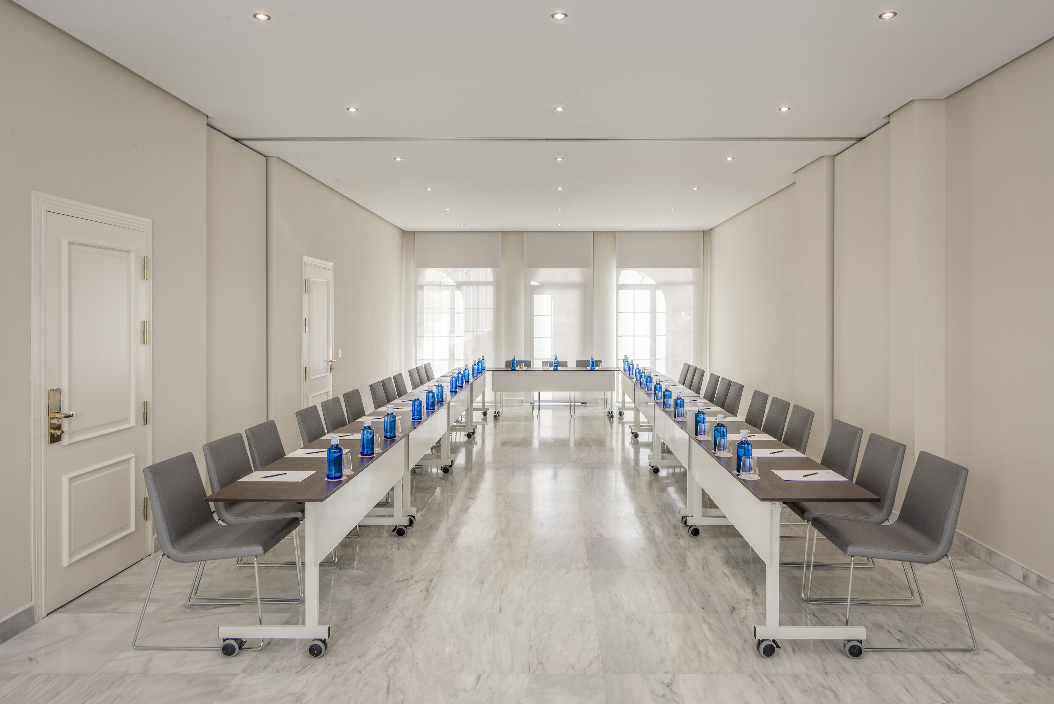Modern U-shape meeting room with grey chairs, blue water bottles, and marble floor.