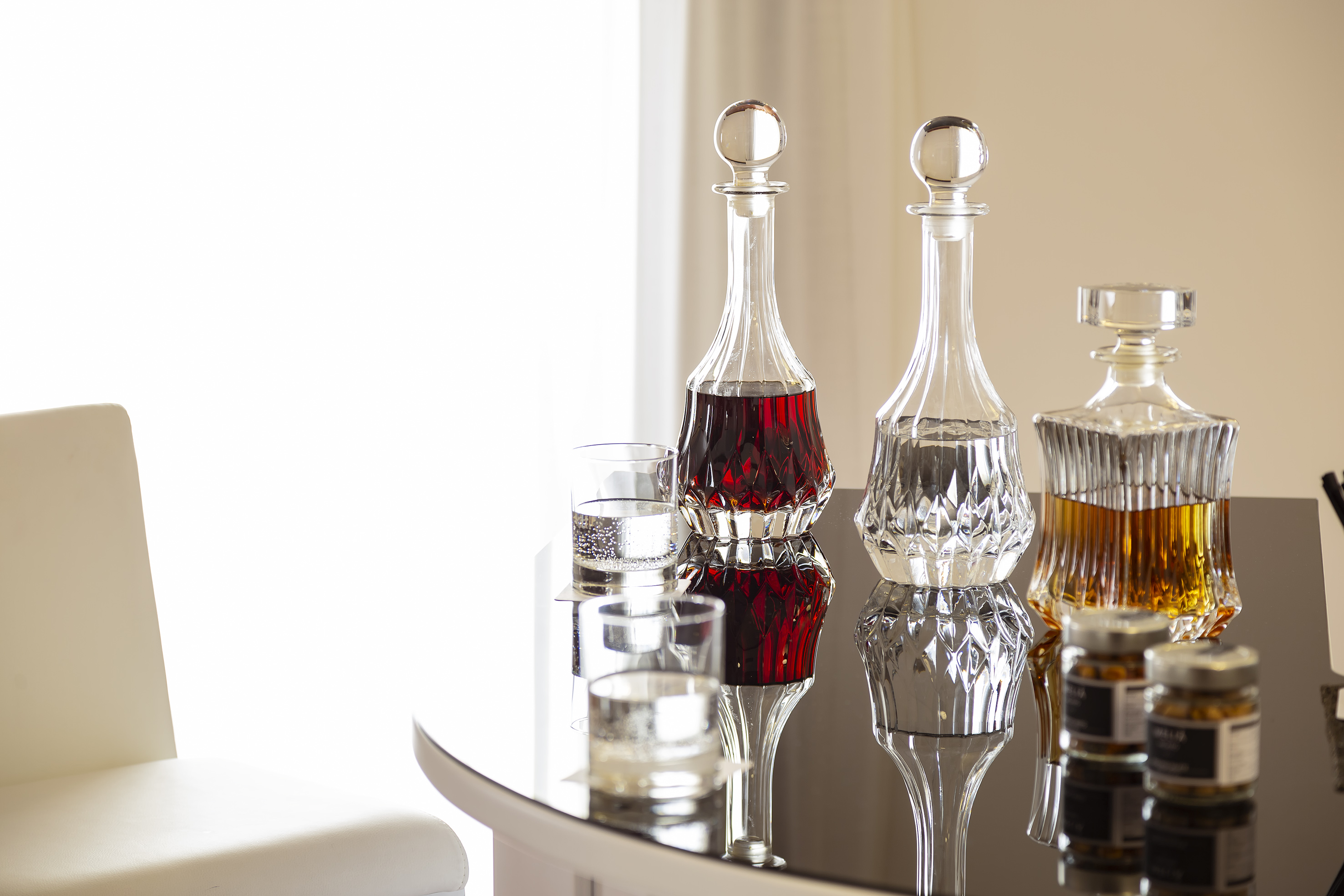 Three crystal decanters with wine, water, and whiskey on a glossy table.
