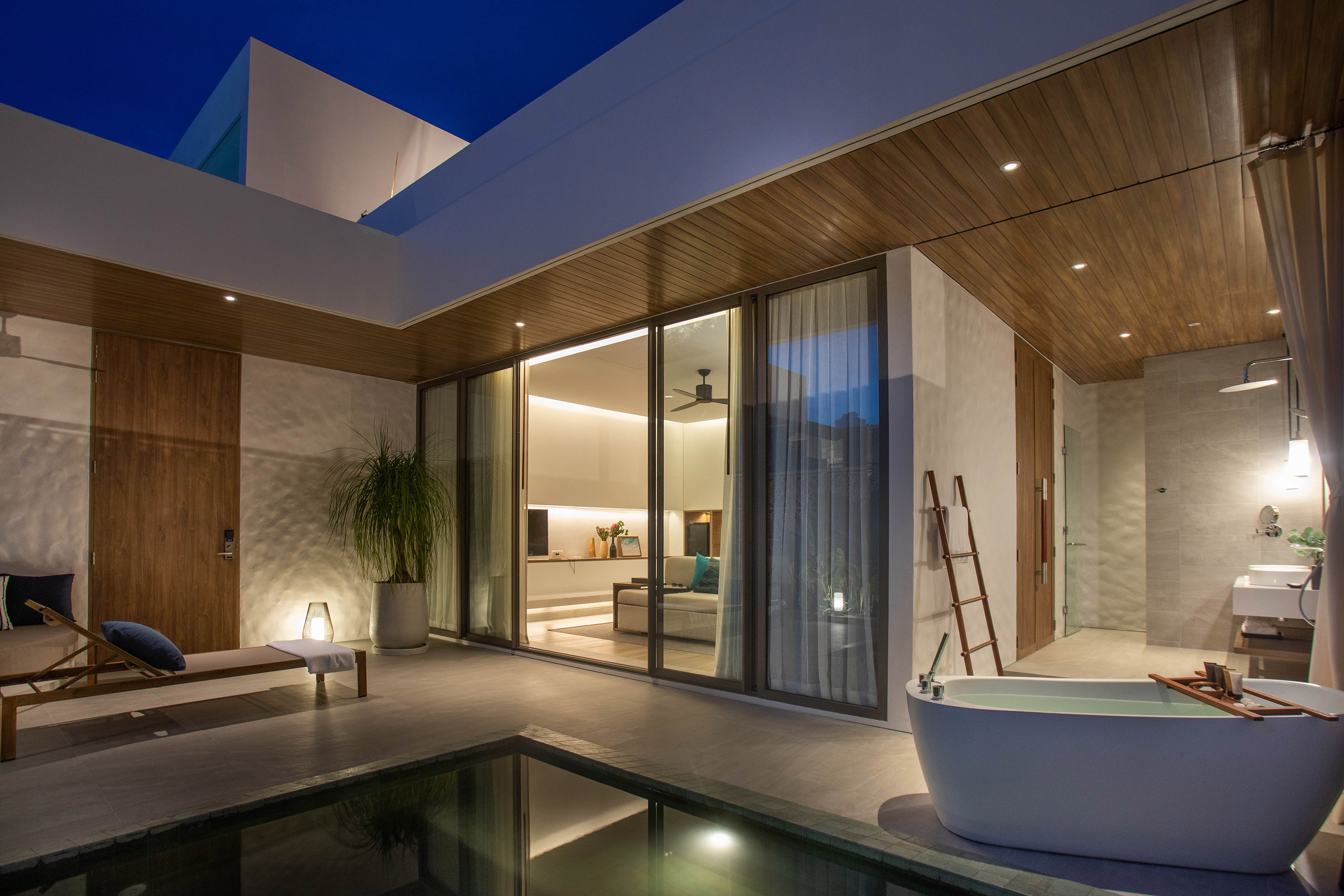 Modern resort villa patio with private plunge pool, outdoor bath, and lounge at night.