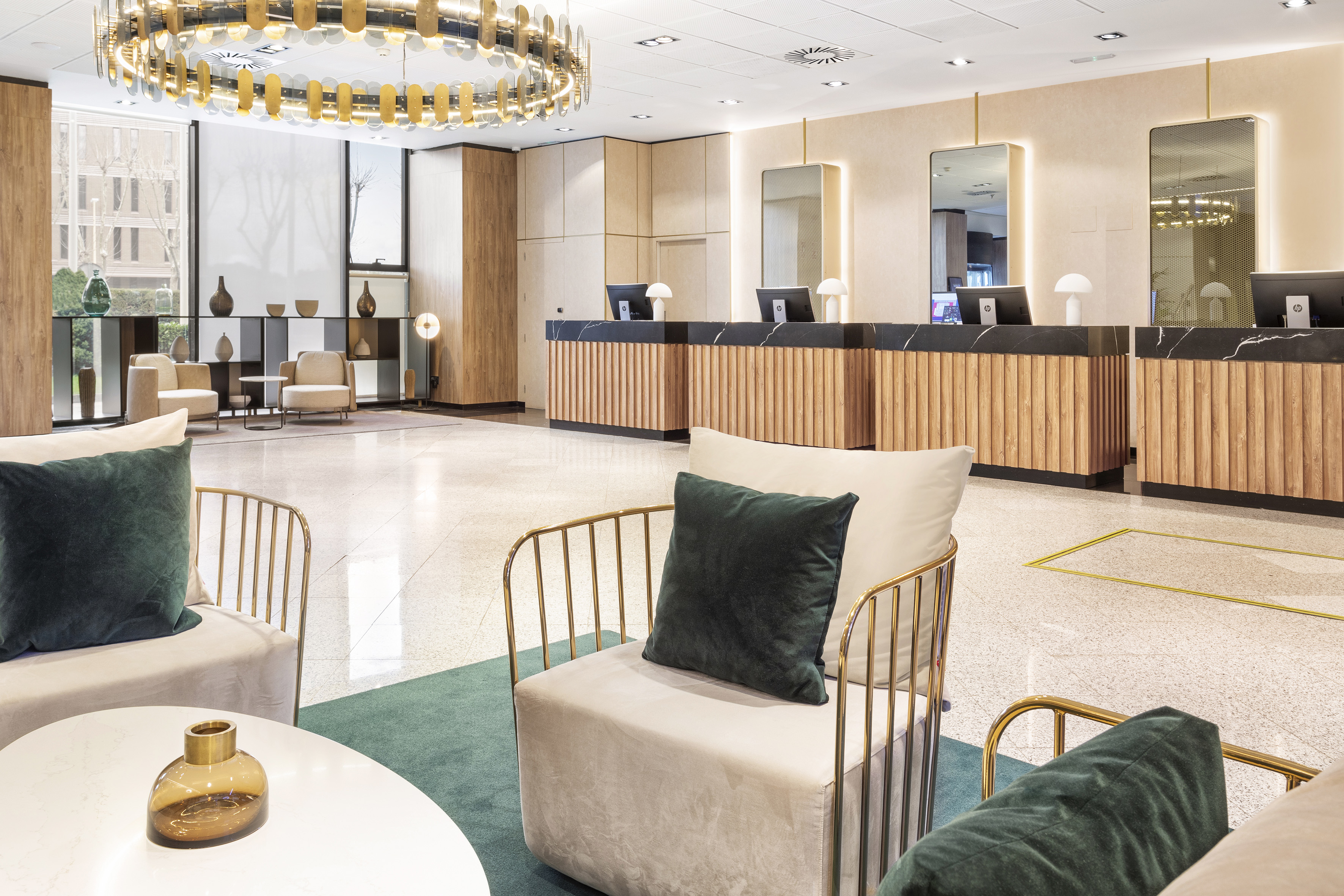 Modern hotel lobby with wood reception desk, lounge chairs, and gold chandelier.