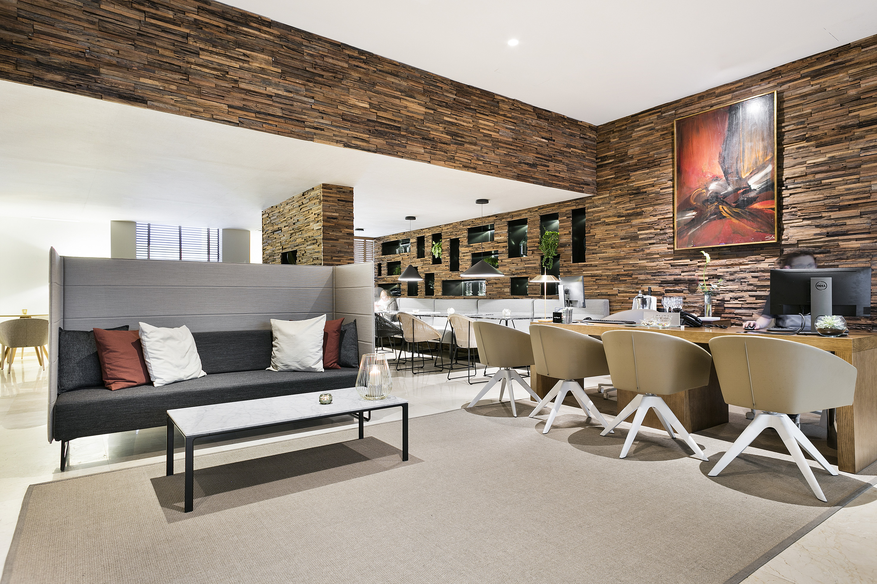Modern hotel reception area with wood panel walls, sofa, and desk.