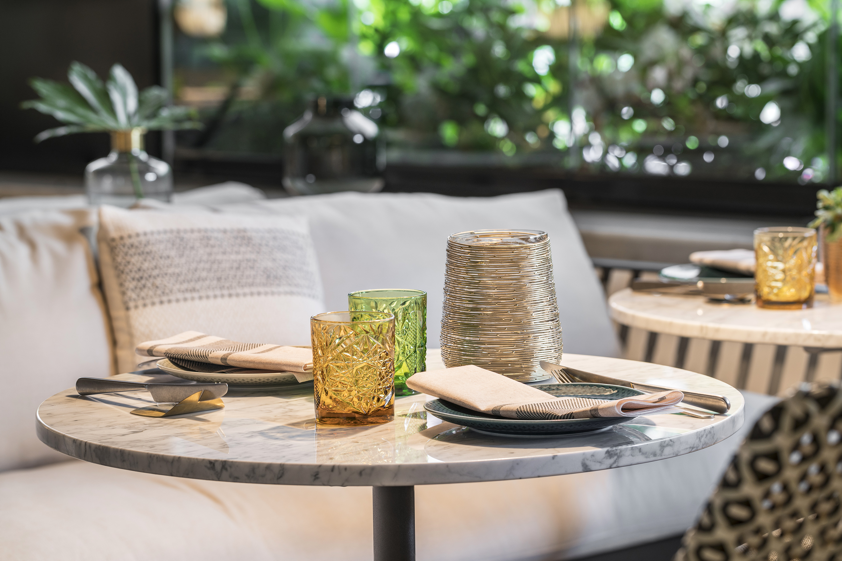 Restaurant marble dining table set with patterned glasses and greenery.