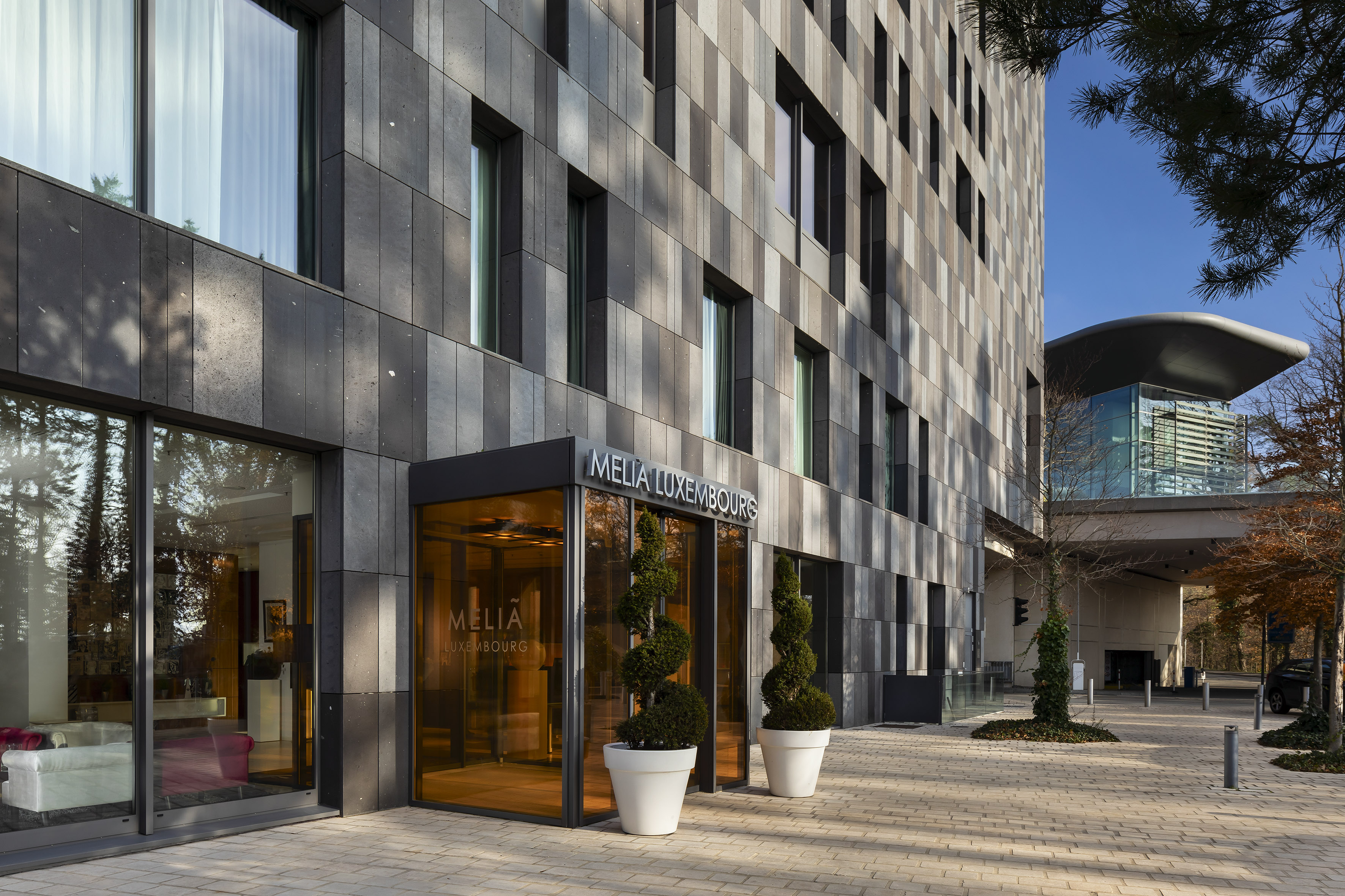 Melia Luxembourg hotel entrance with modern facade and spiral topiaries.