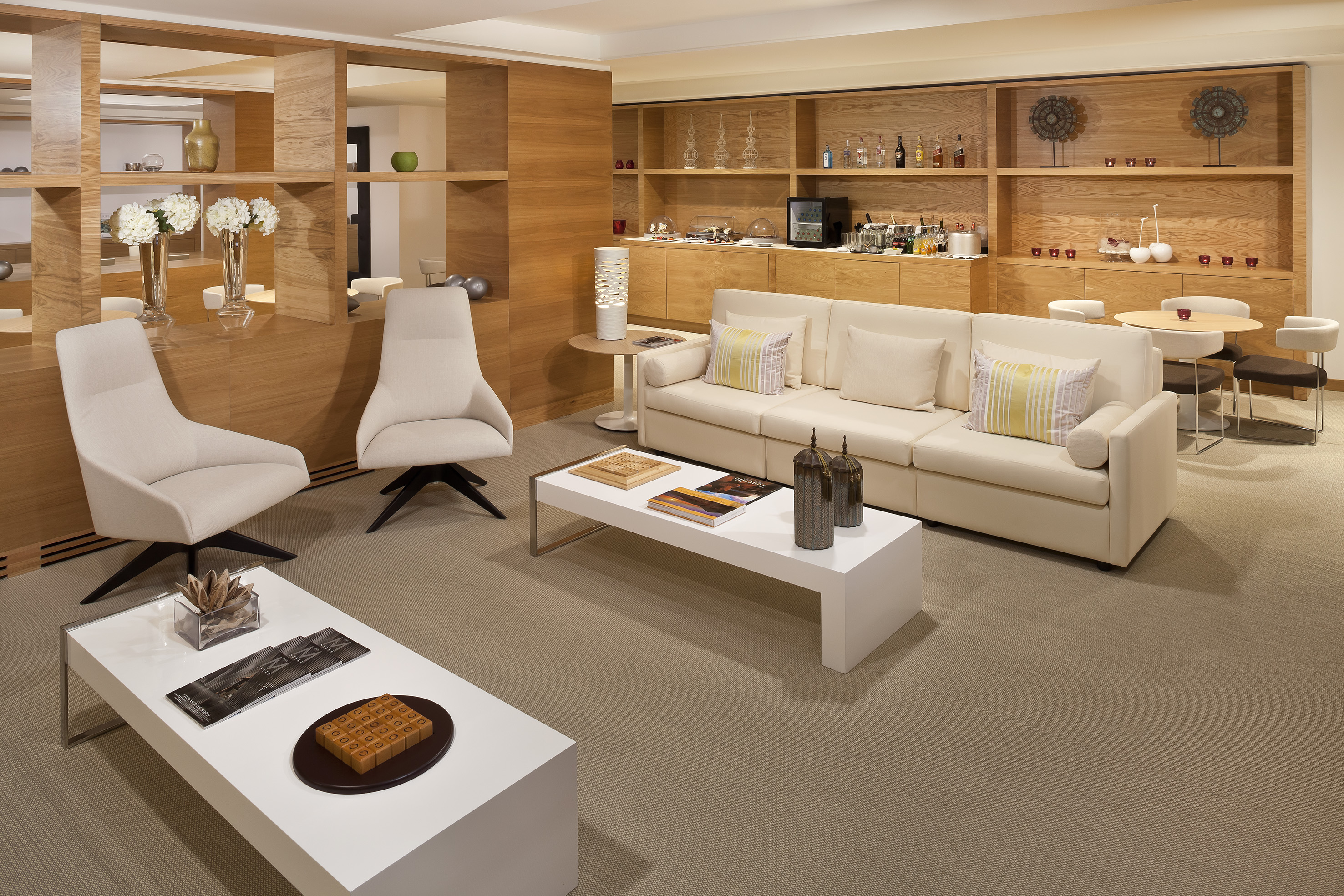 Contemporary hotel lounge with cream seating, wooden accents, and refreshment bar.