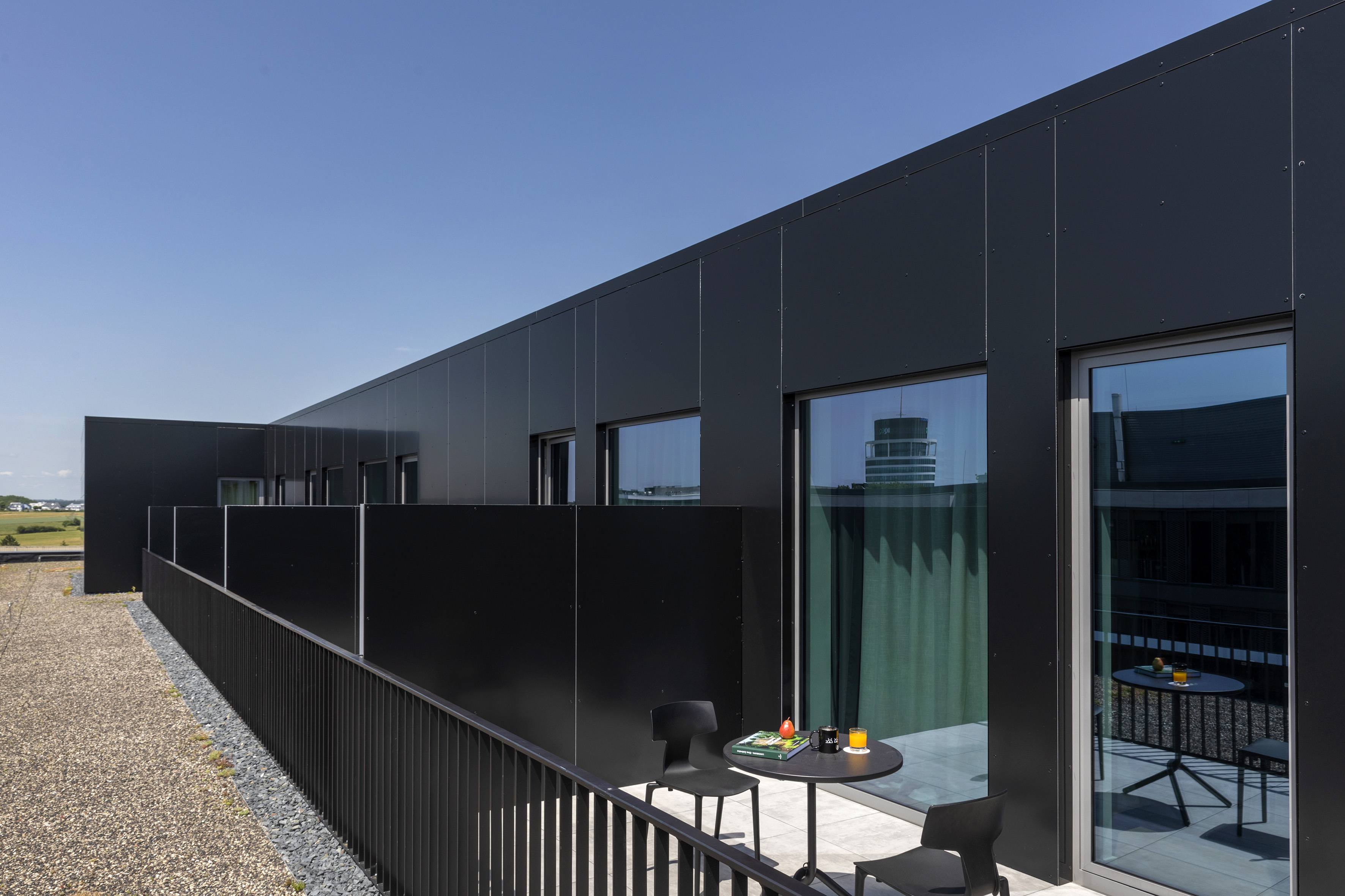 Modern black facade building with private balcony, outdoor table and chairs.