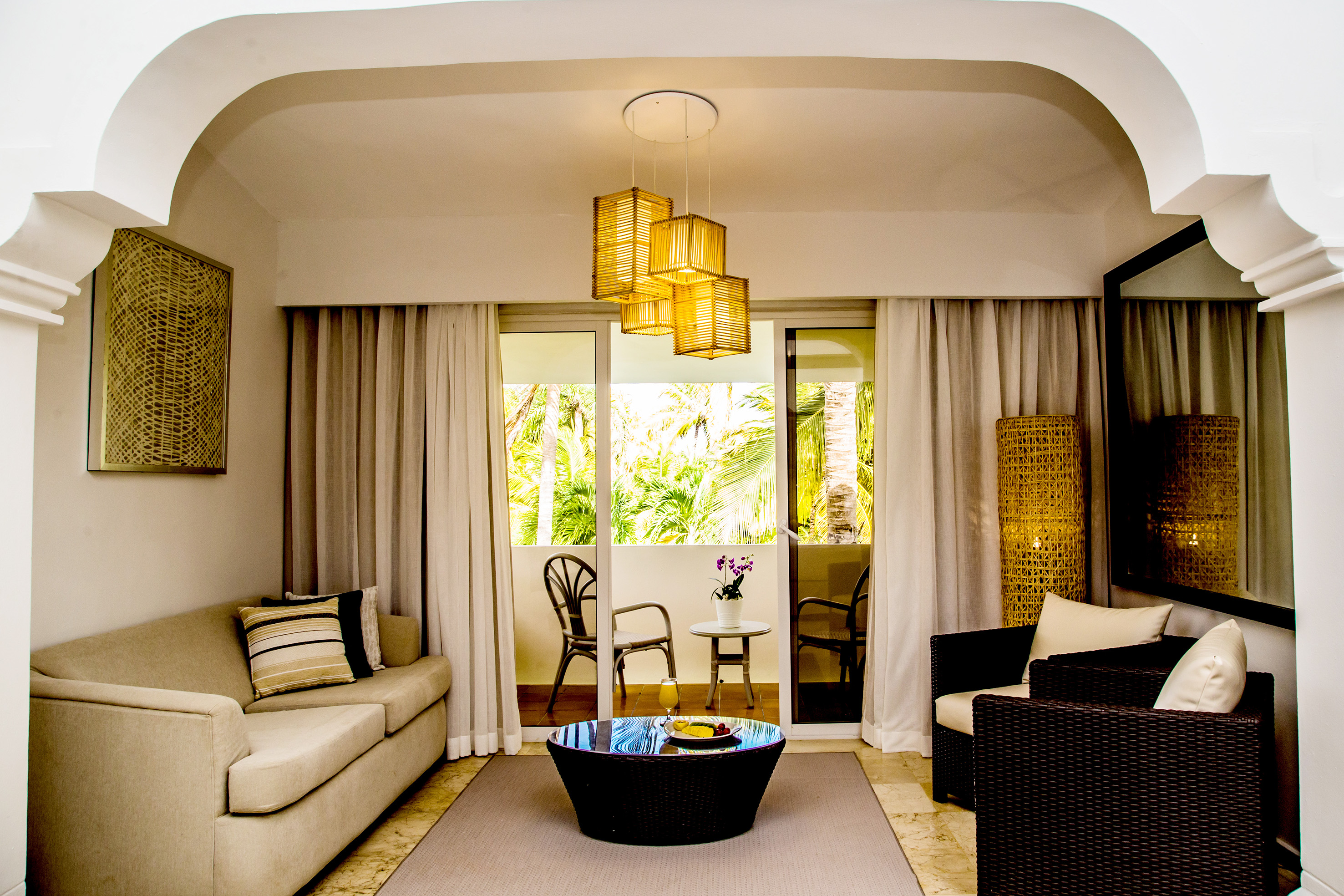 Tropical hotel suite living room with balcony and lush palm view.