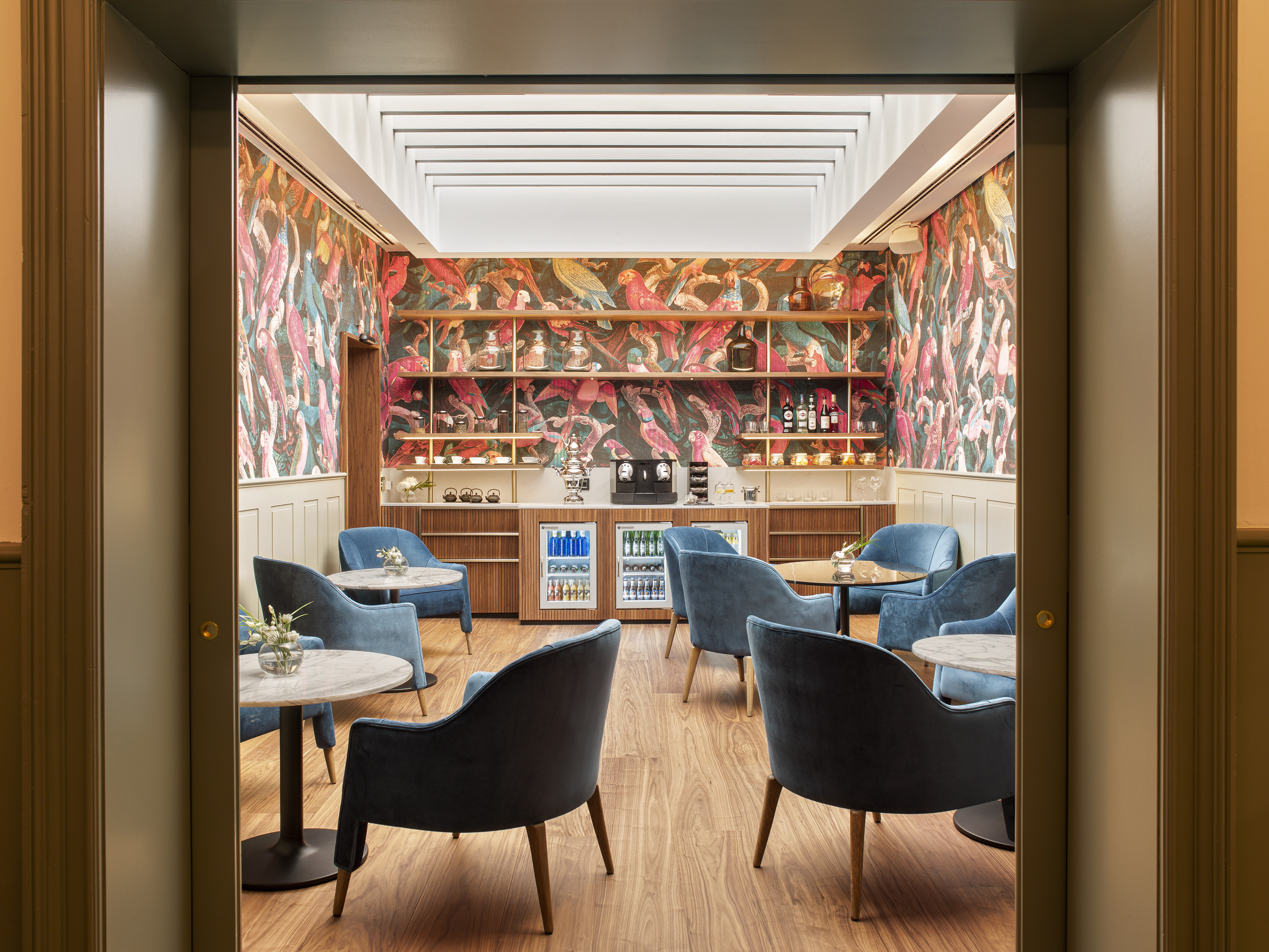 Lounge with blue velvet chairs, exotic bird wallpaper, and refreshment bar.