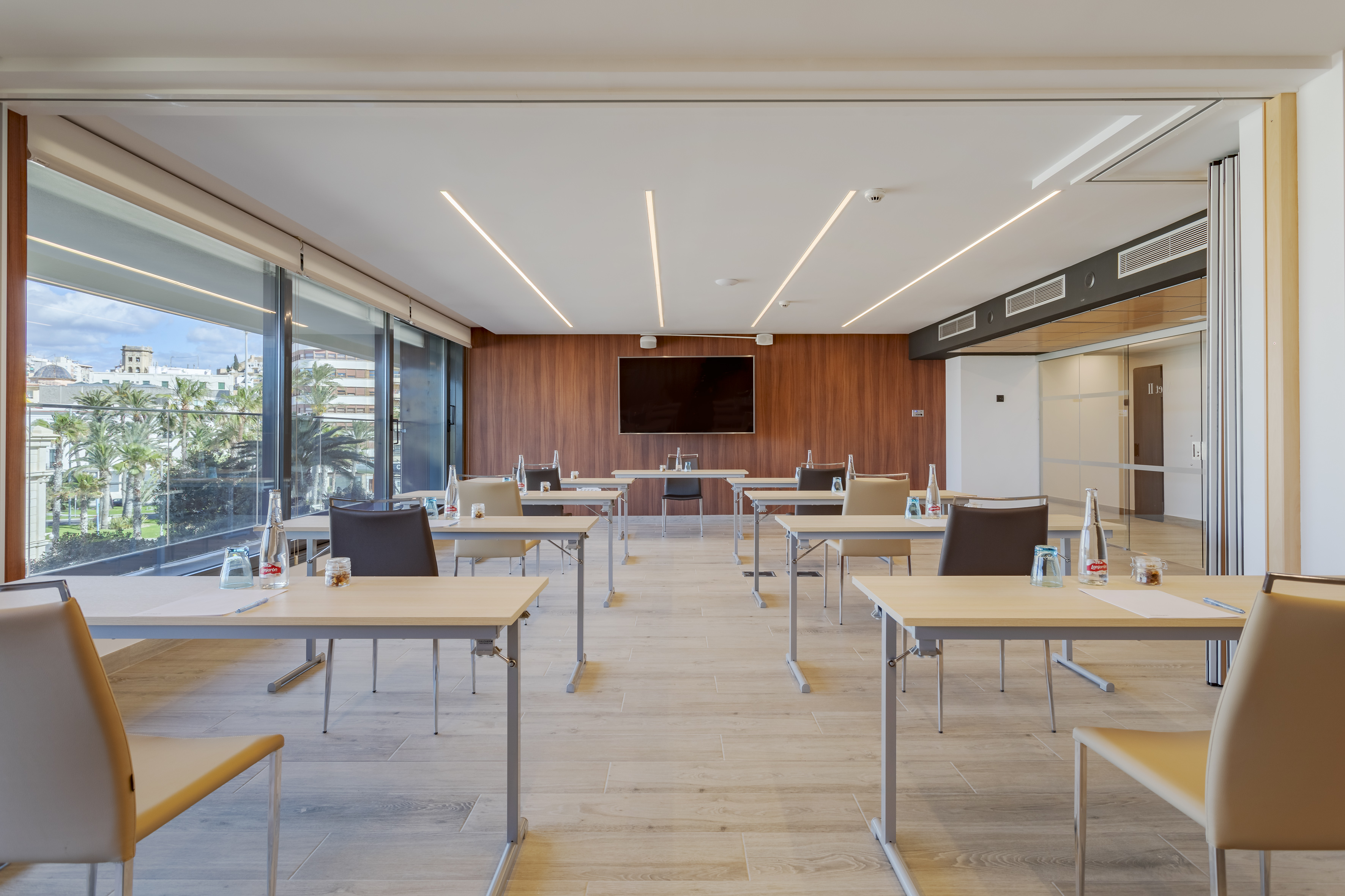 Modern conference room with city view, presentation screen, tables, and chairs.