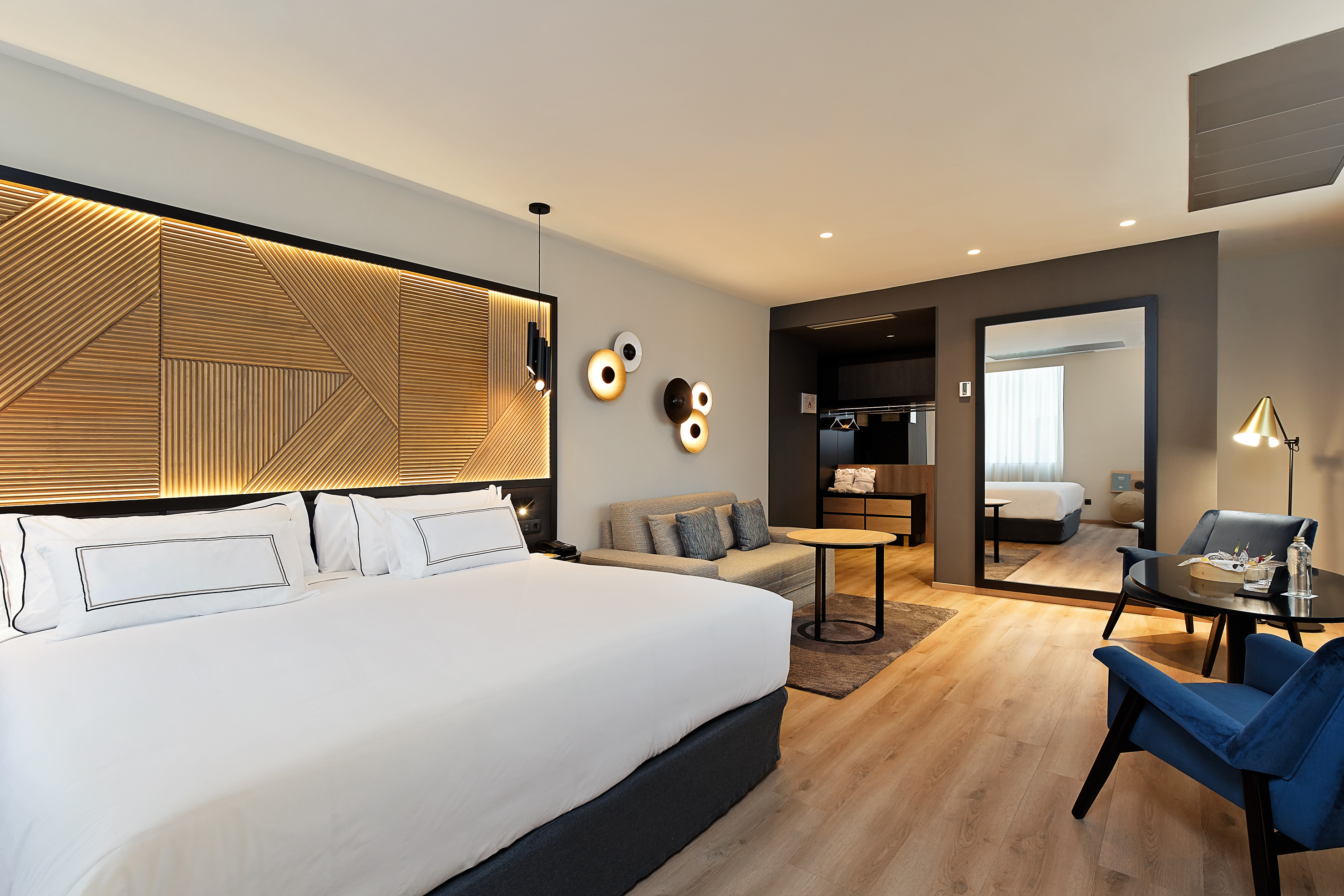 Contemporary hotel suite with large bed, sofa, and elegant seating area.