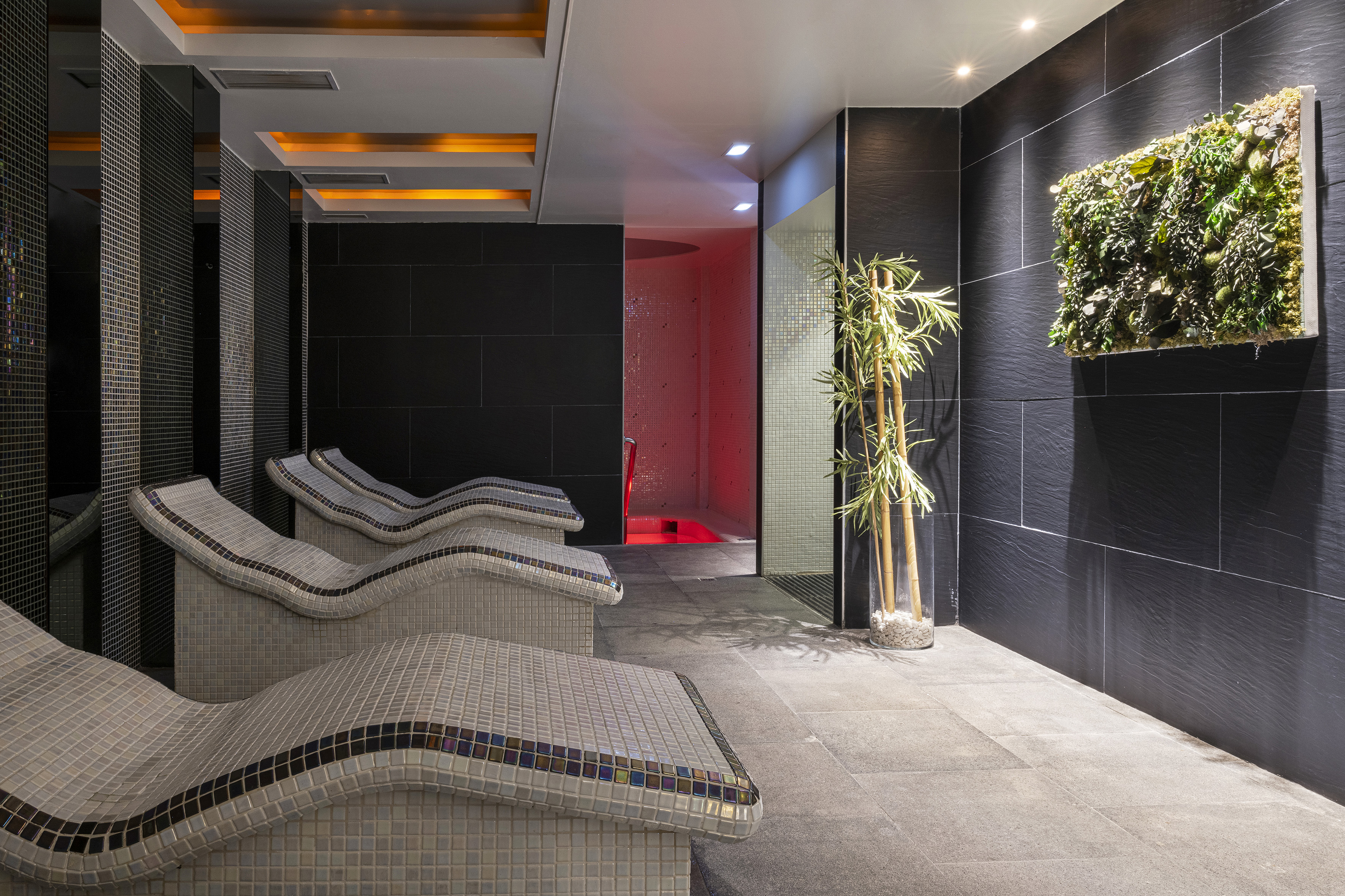 Modern spa with mosaic loungers, vertical garden, and red-lit wellness area.
