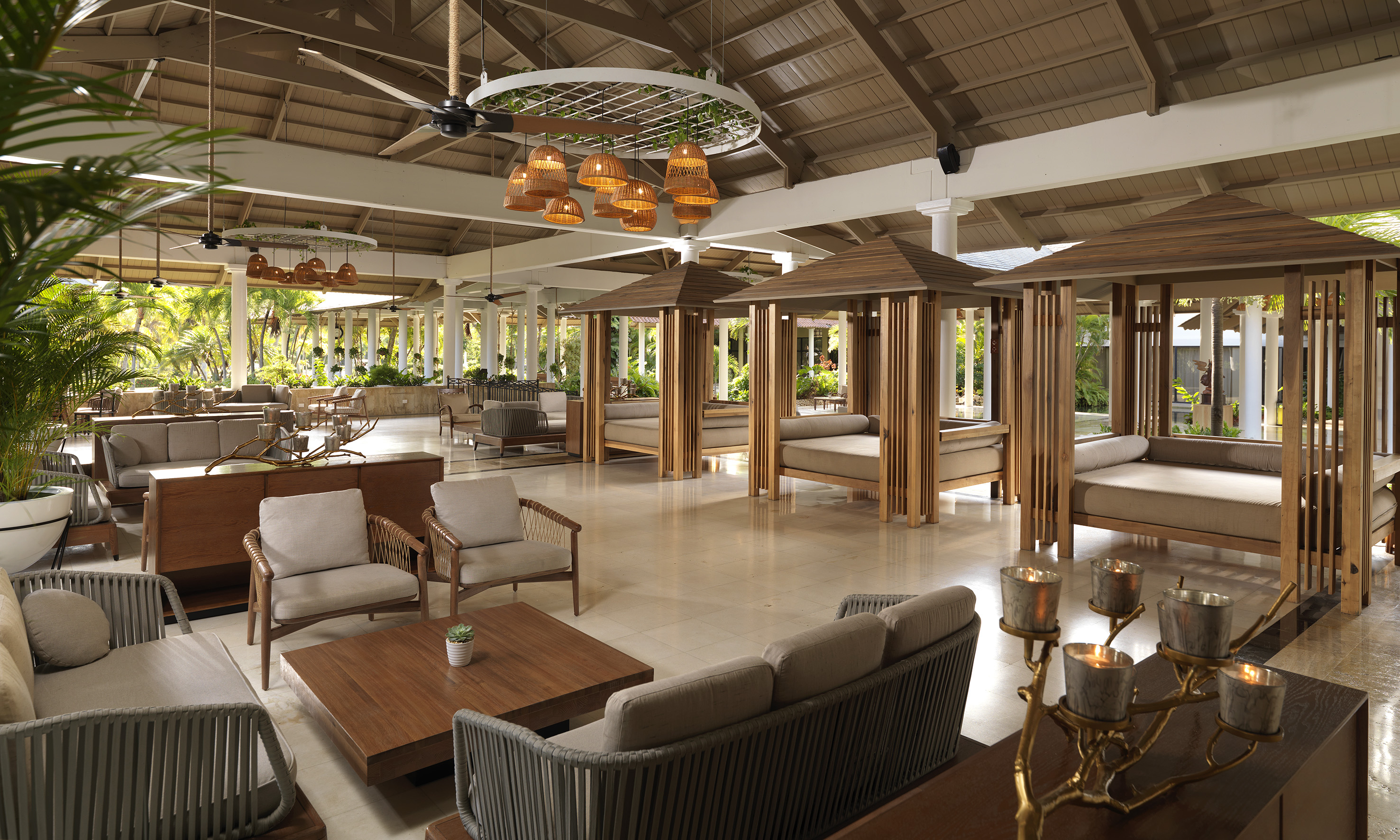 Tropical resort lounge with wooden daybeds, rattan seating, and high ceilings.