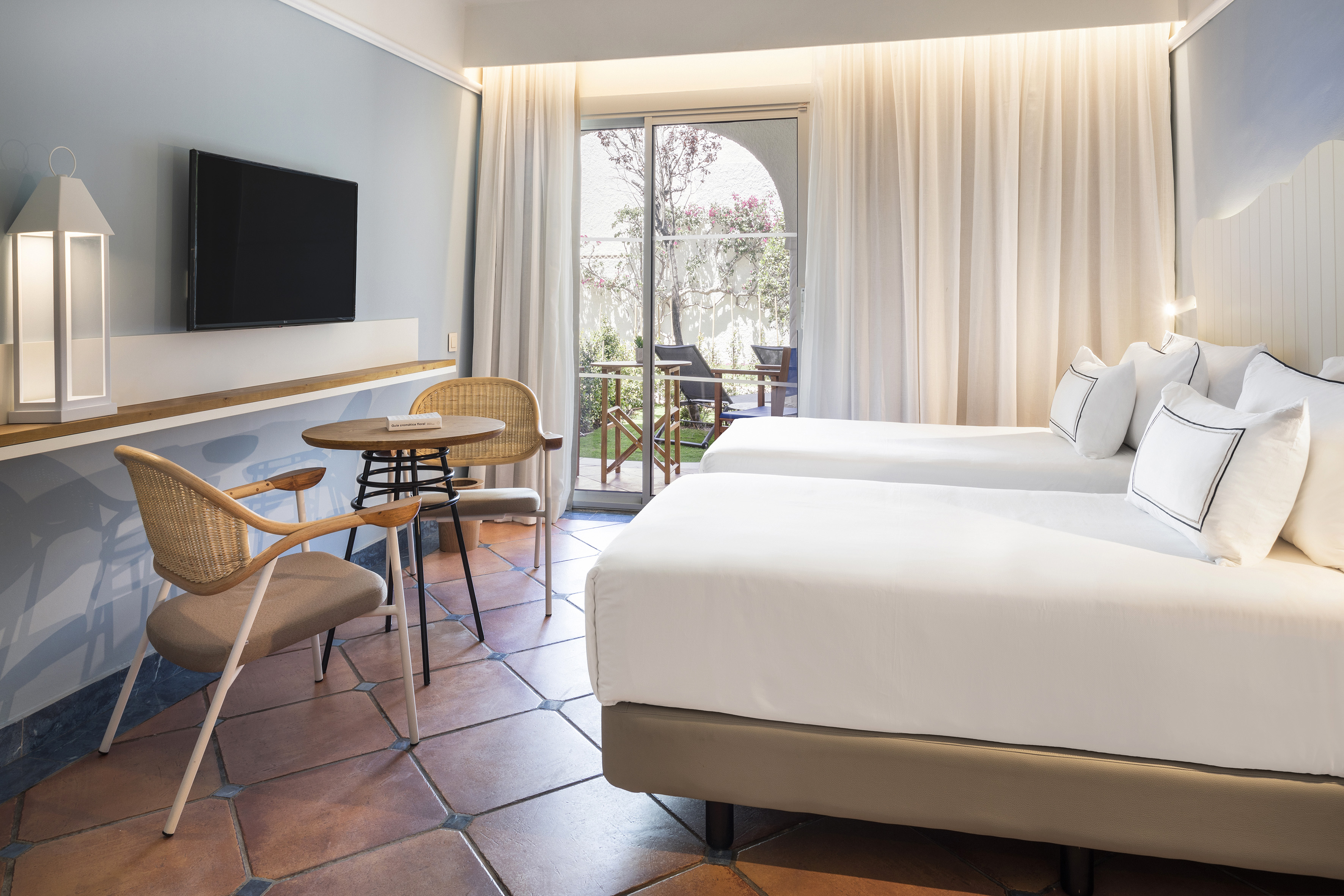 Modern resort room with twin beds, terracotta floor, TV, and patio access.