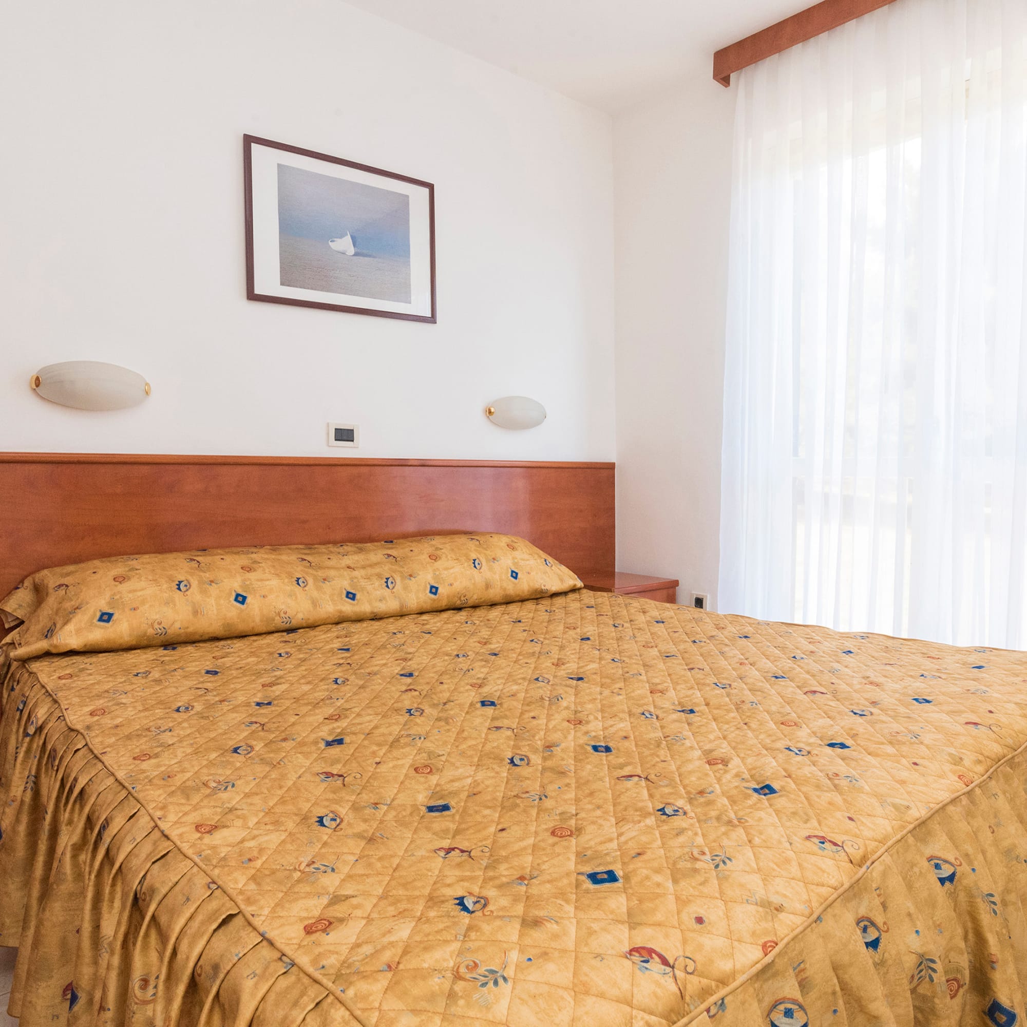 a bed with a gold blanket and a picture on the wall