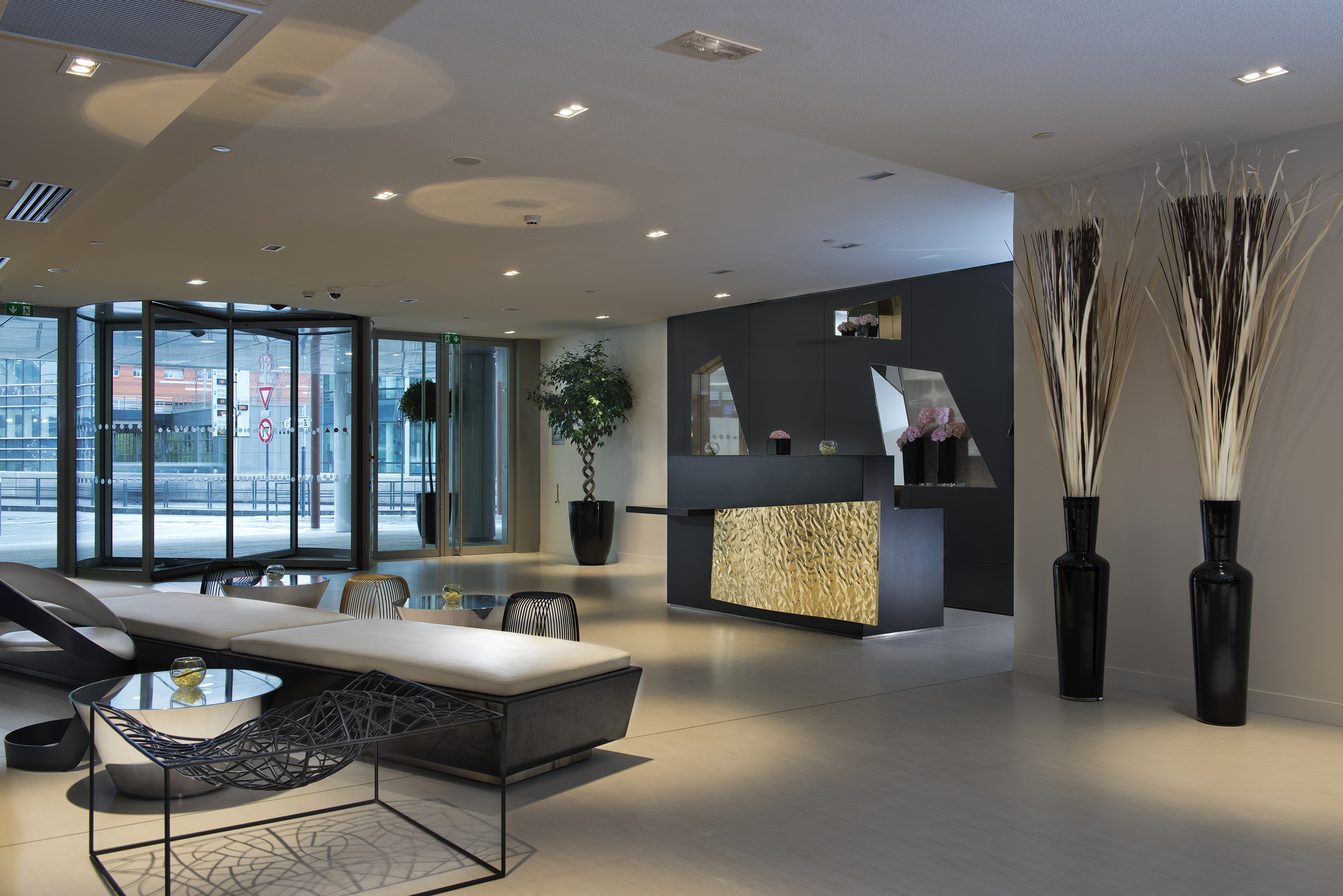 Modern hotel lobby with gold reception desk, lounge, and glass entrance.