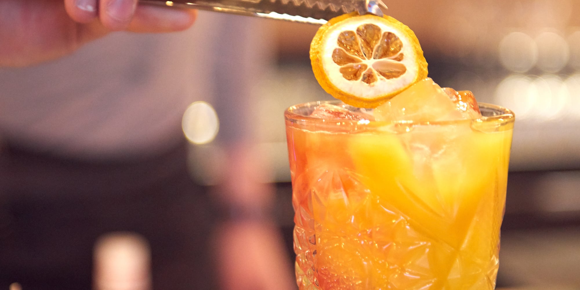 a person holding a lemon slice over a glass of liquid