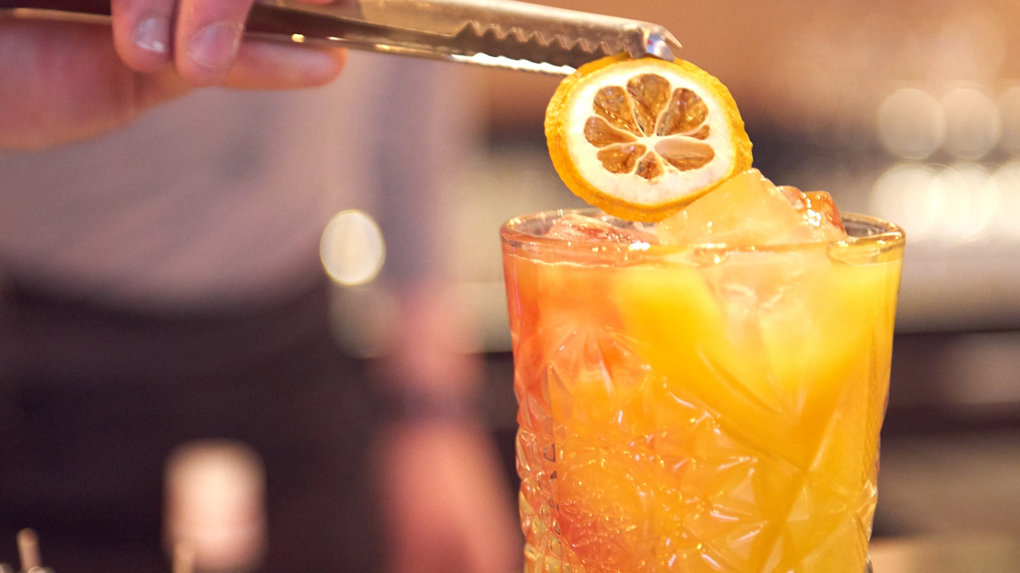 a person holding a lemon slice over a glass of liquid
