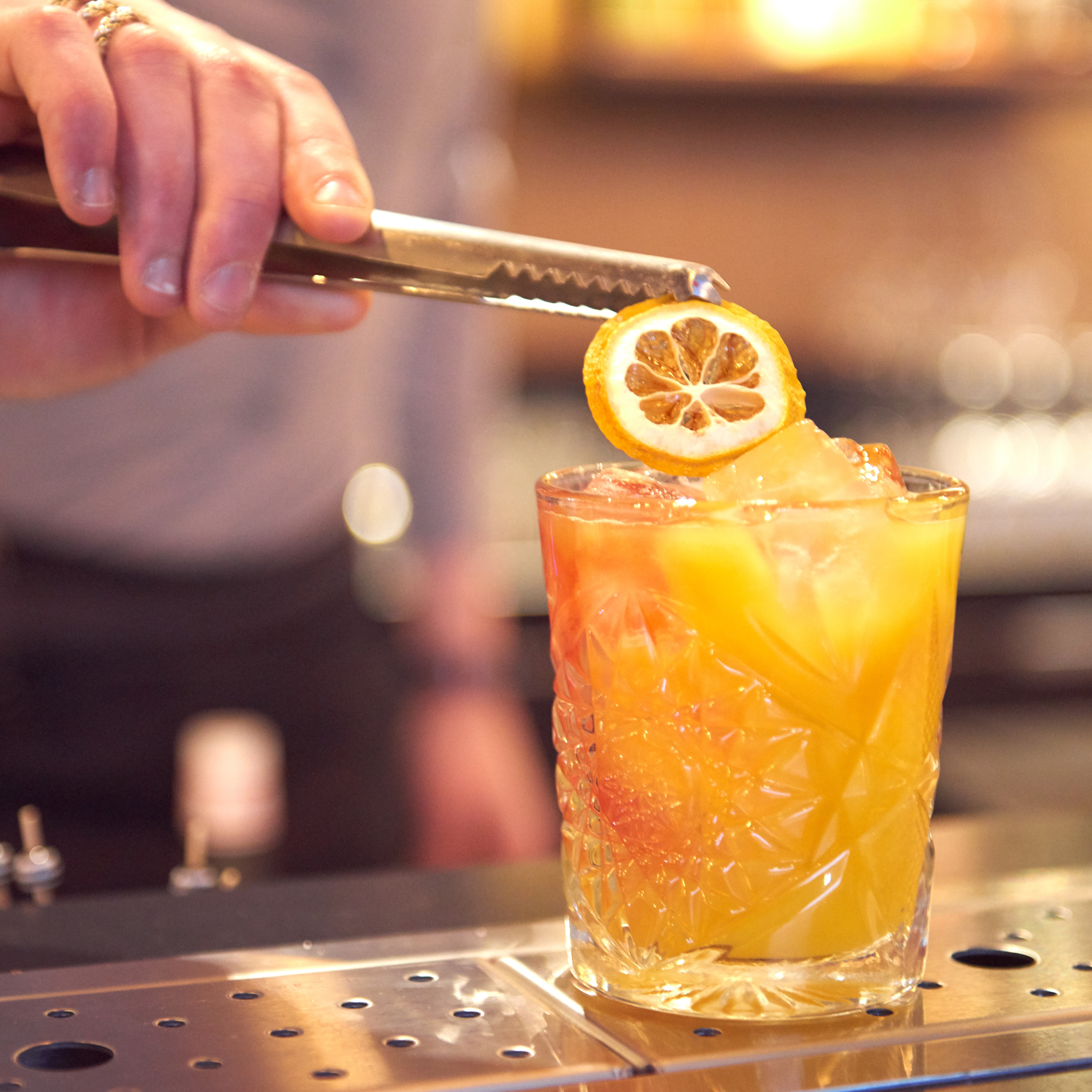 Bartender garnishing a vibrant orange cocktail with a dried orange slice.