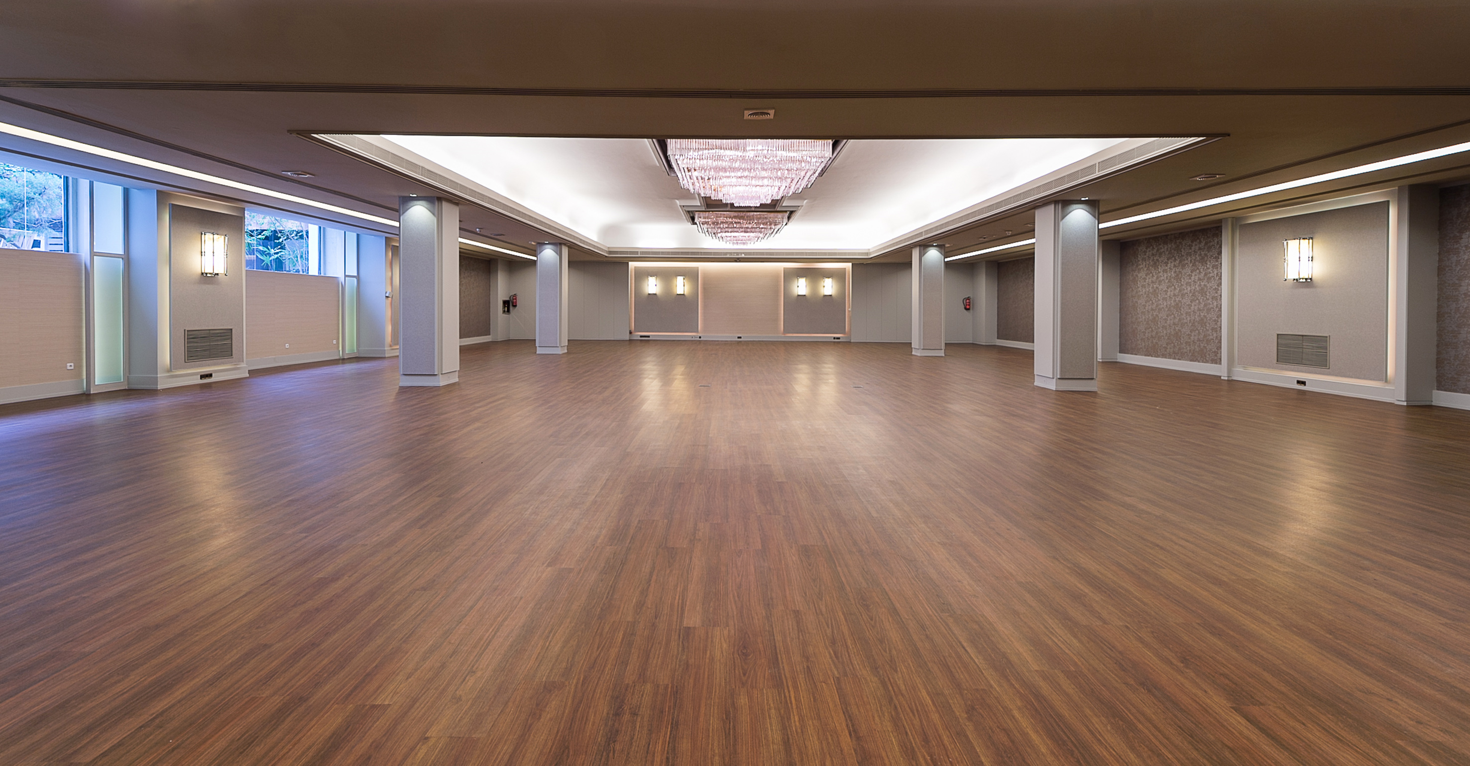 Modern empty event venue with wood floor, chandeliers, and large windows.