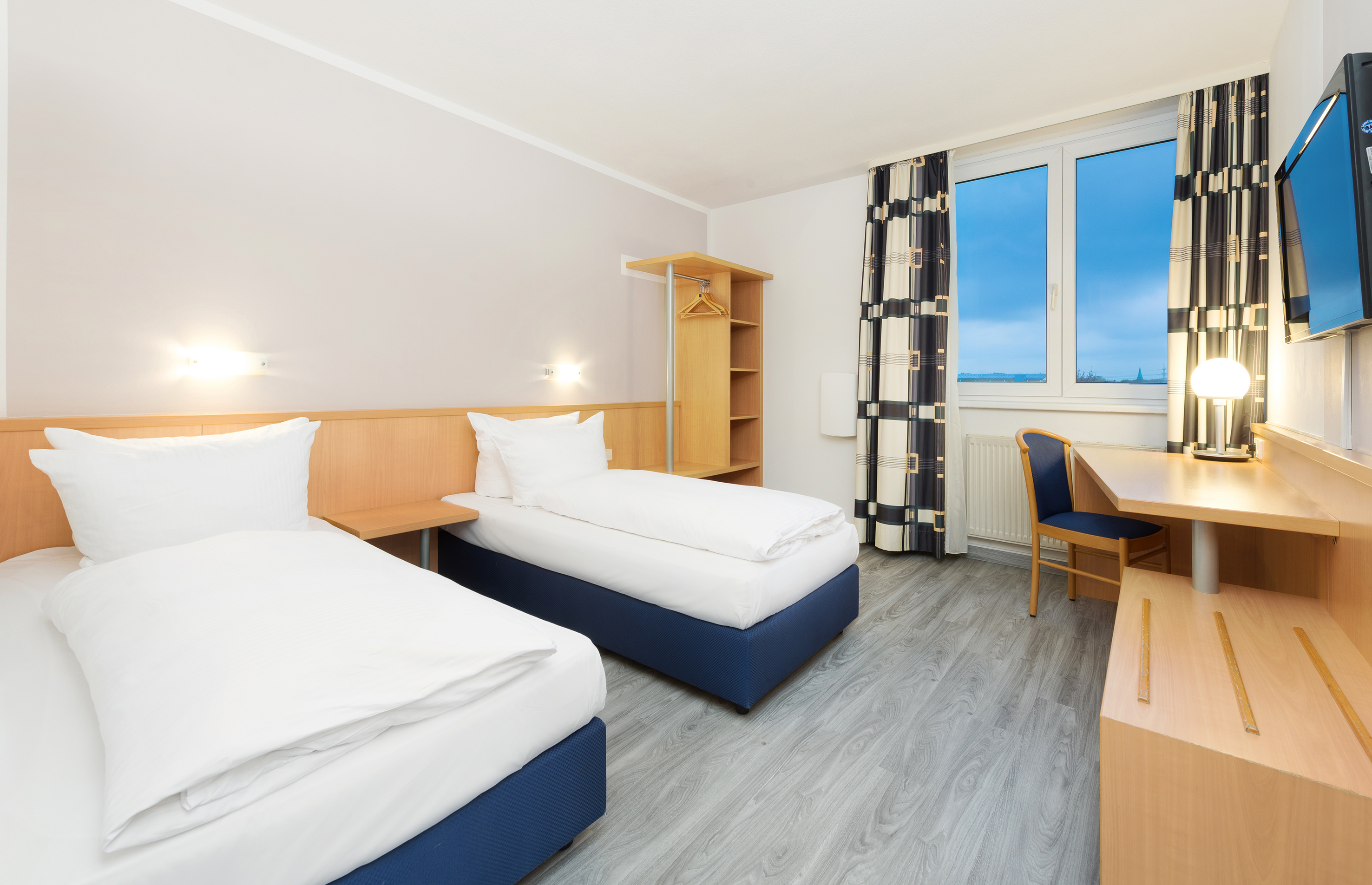 Twin hotel room with two single beds, wooden desk, and modern decor.