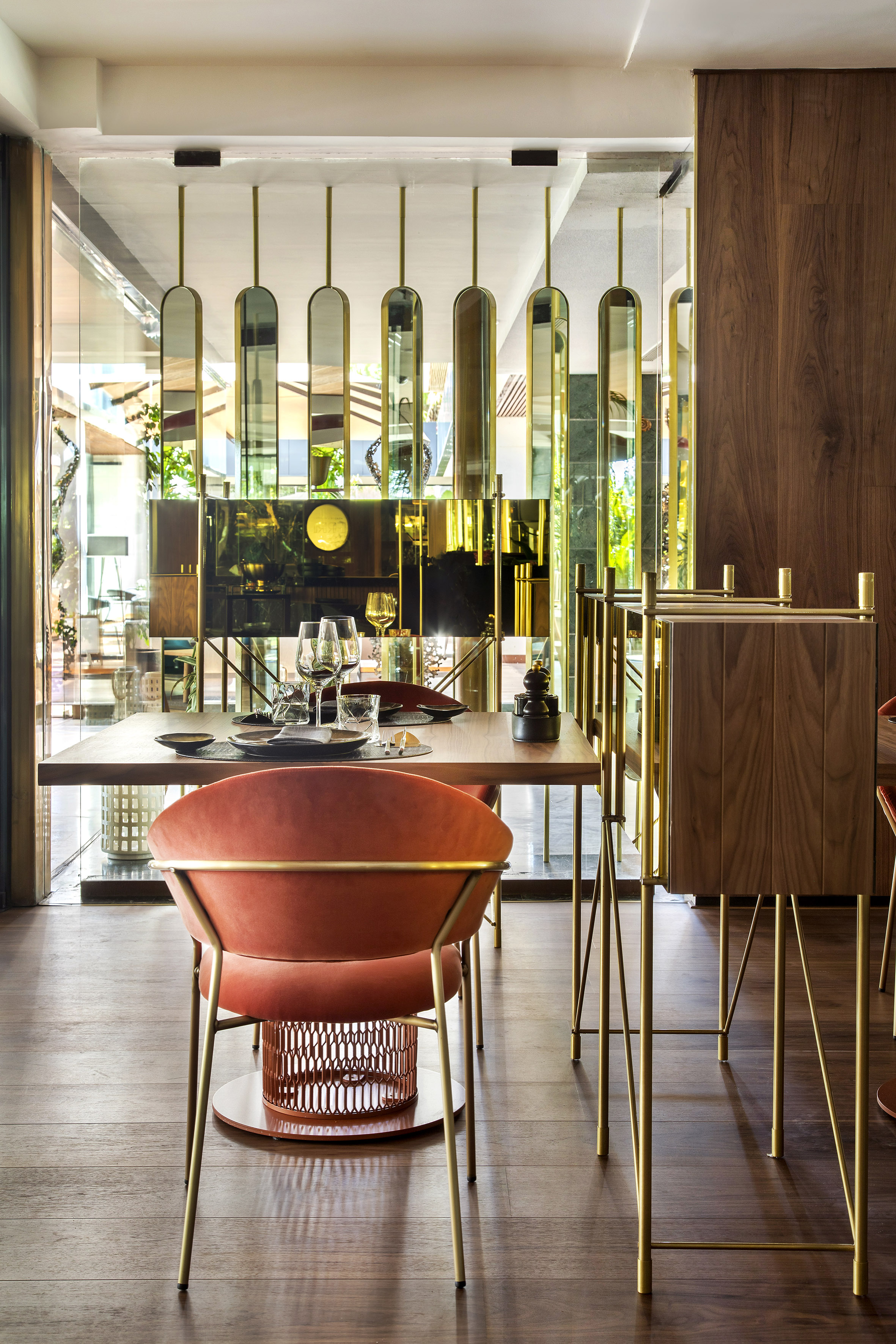 Luxury dining room: coral velvet chairs, wood table, and brass decorative screens.