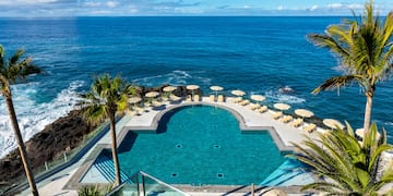 a swimming pool with chairs and umbrellas by the ocean