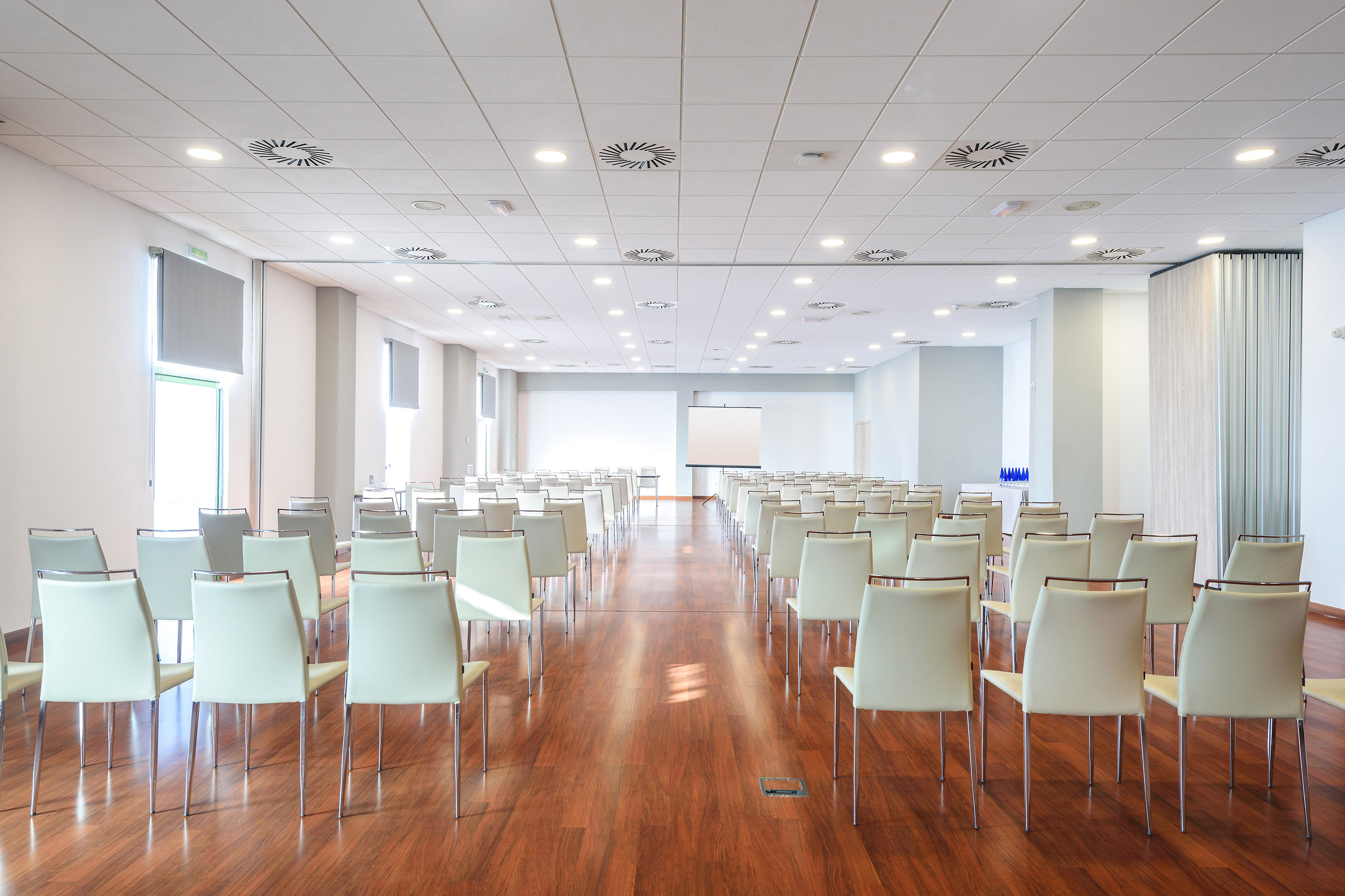 Empty modern conference room with rows of chairs, wooden floor, and projector screen.