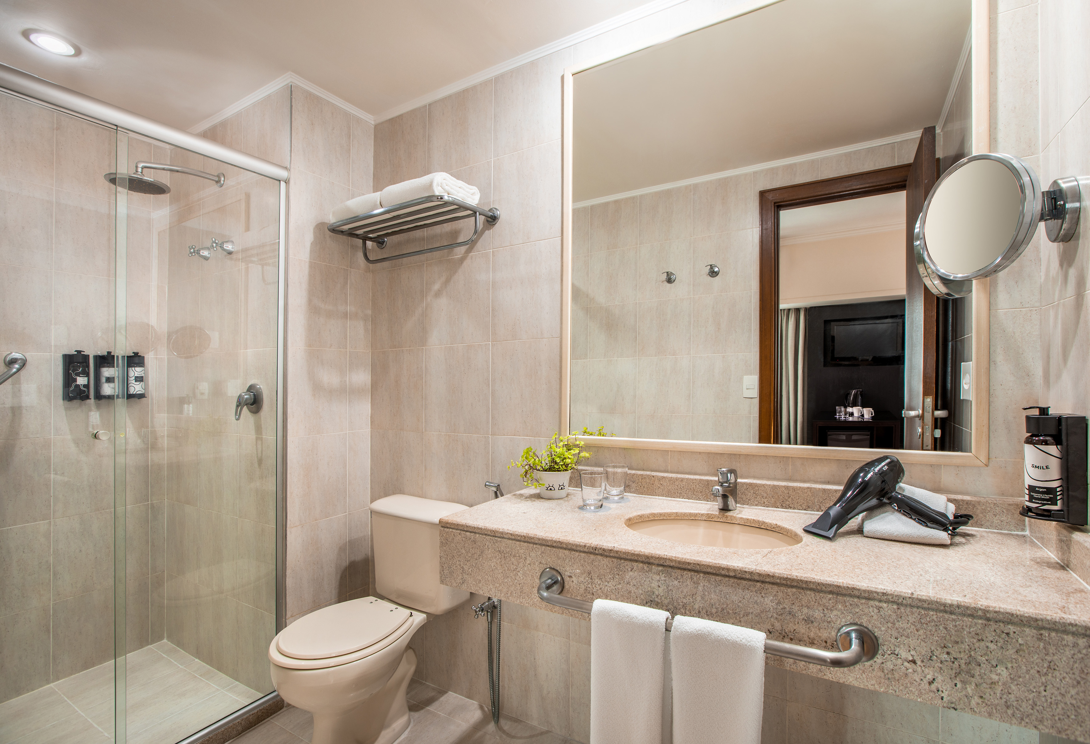 Neutral hotel bathroom with glass shower, toilet, and granite vanity sink.