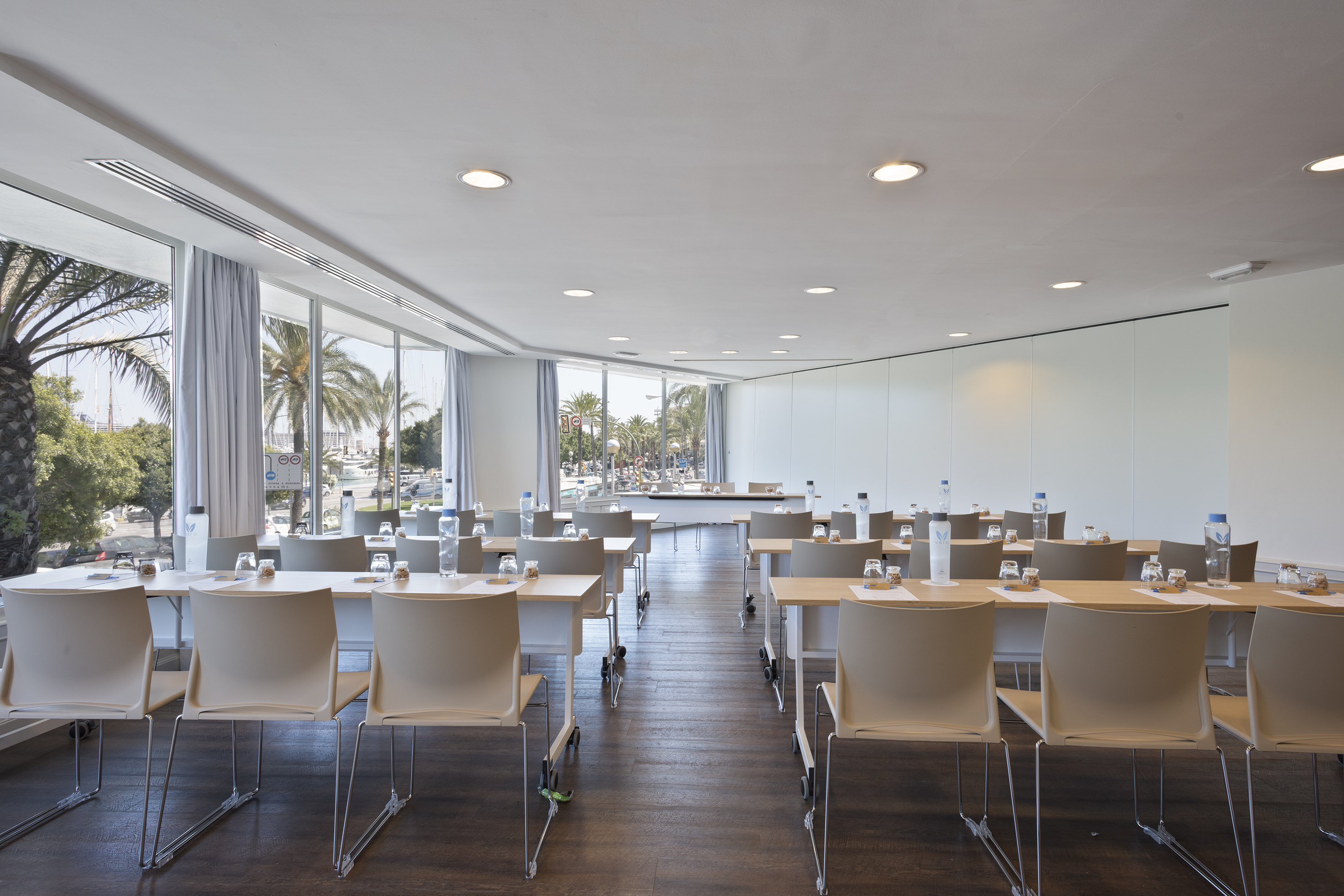 Modern meeting room with natural light, rows of tables, and palm tree view.
