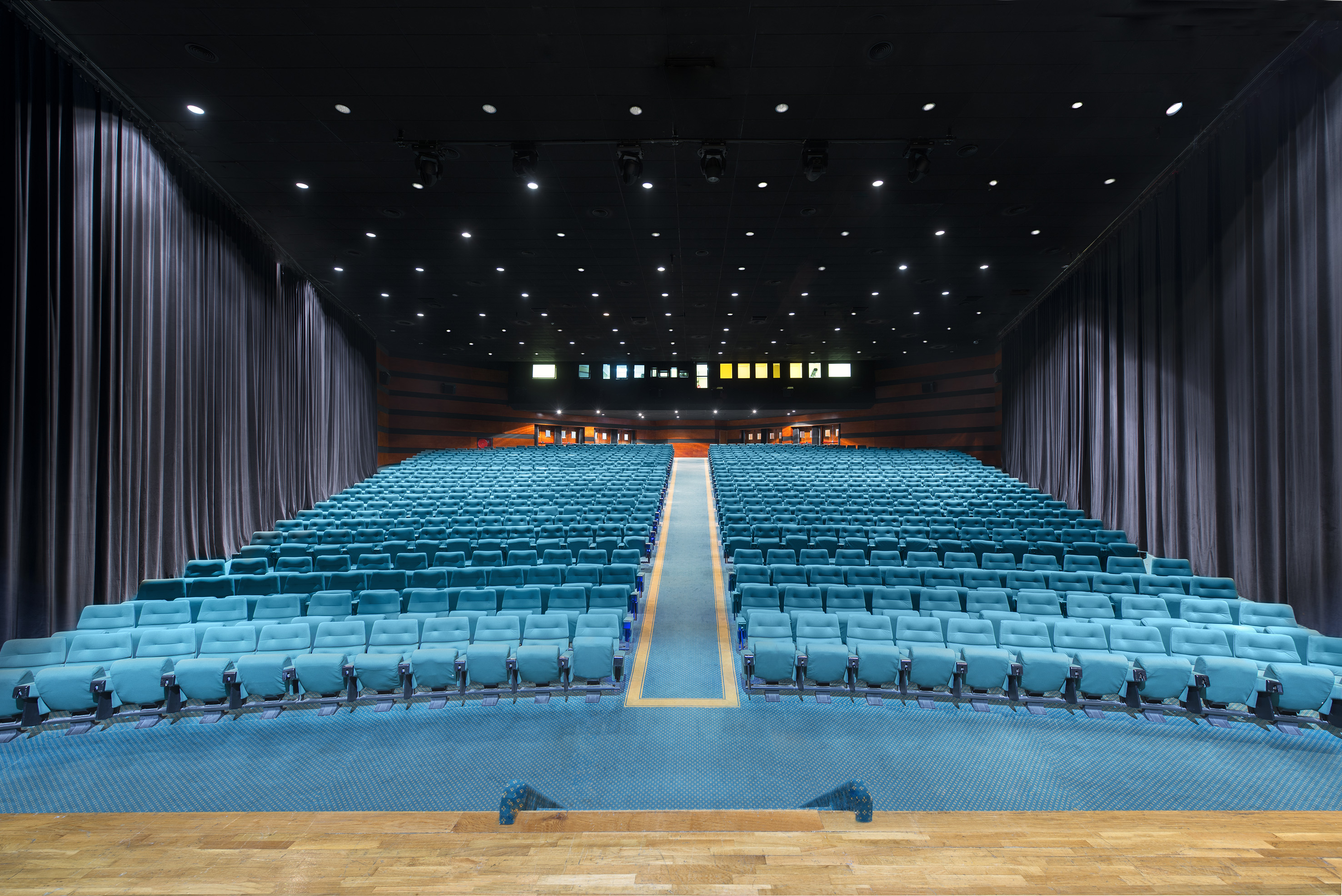 Large empty auditorium with rows of blue theater seats and a wooden stage.