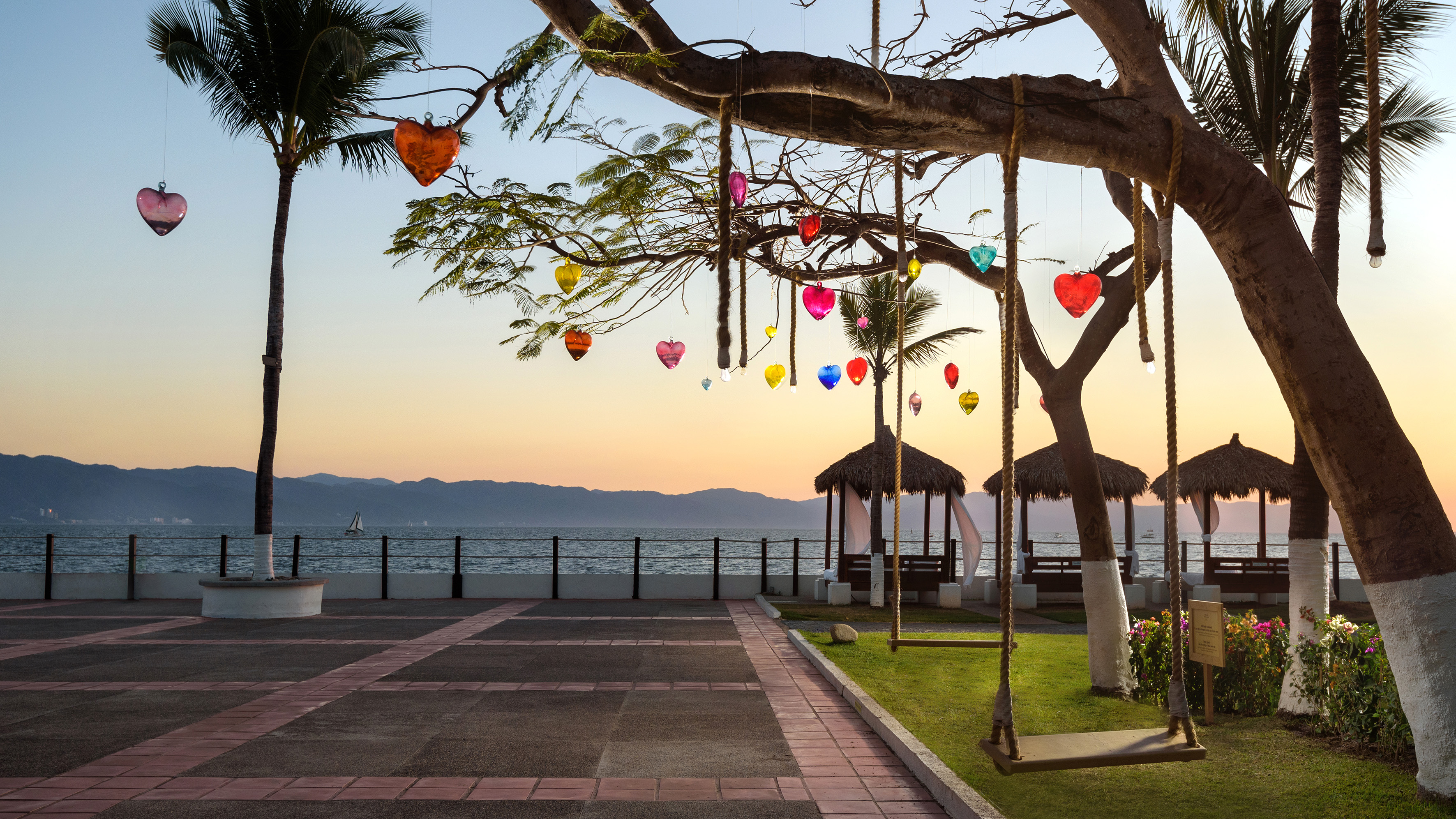 Sunset beach with colorful heart lanterns, tree swings, and ocean.