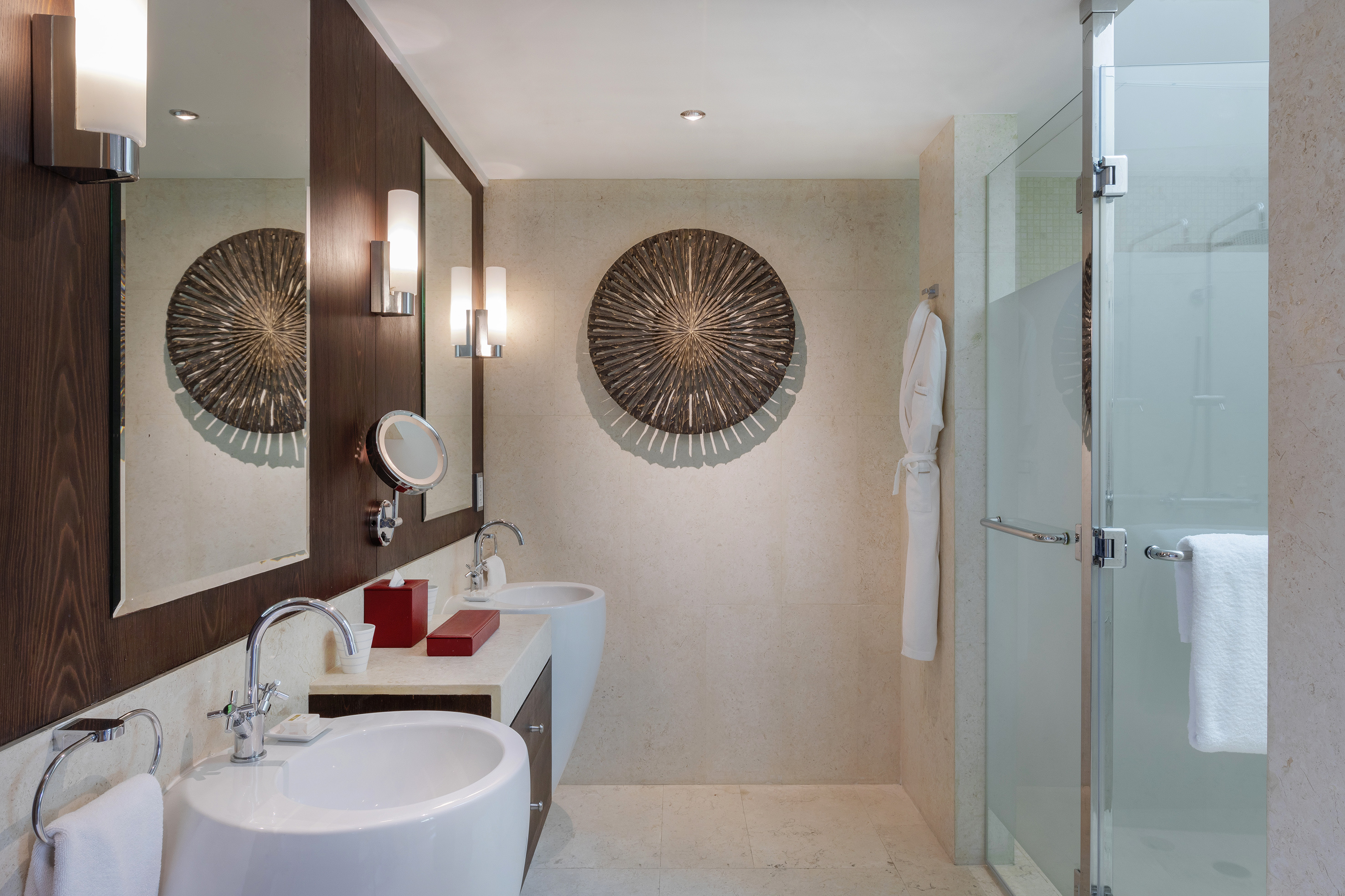 Modern bathroom with double vanity, dark wood accents, circular wall art, glass shower.
