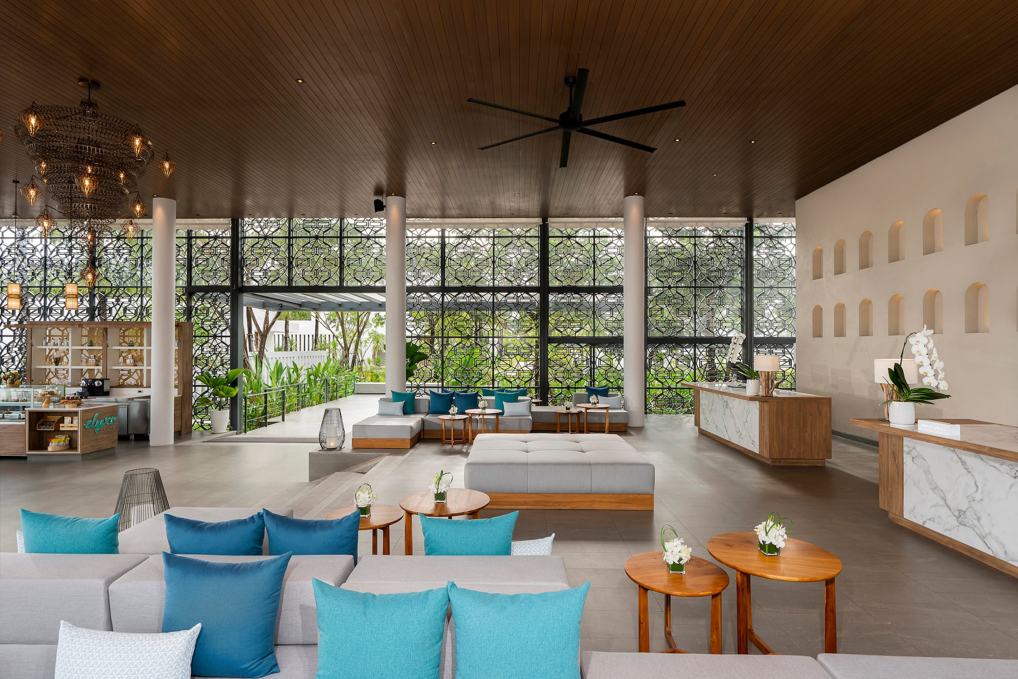 Stylish tropical hotel lounge with blue sofas, wooden tables, and patterned windows.